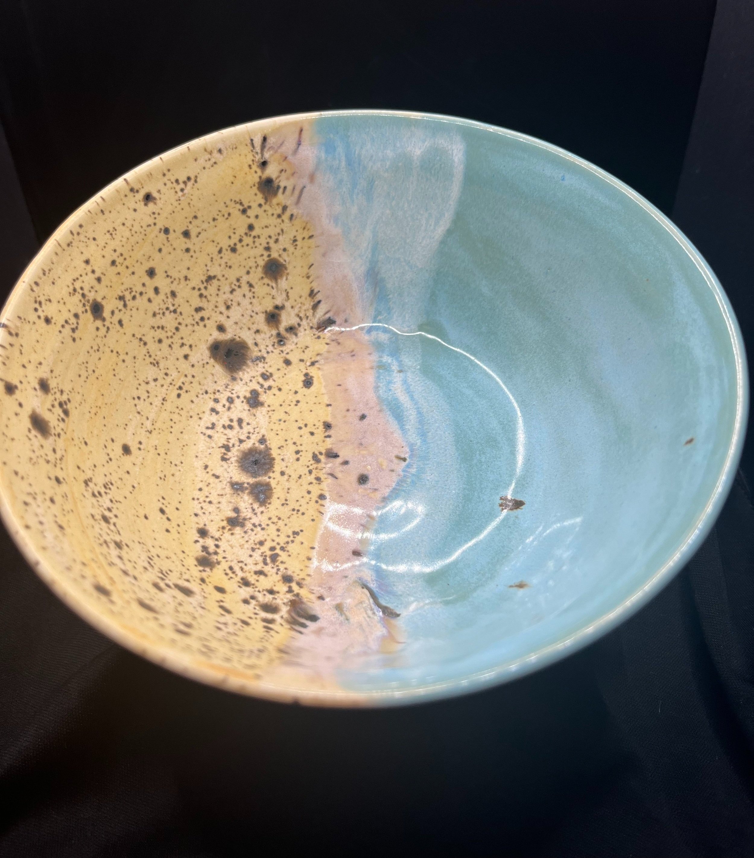 Thomika Segar Artist Pottery. A ceramic bowl with a glaze resembling a beach scene, featuring blue water, pink sand, and a yellowish sky with black spots.