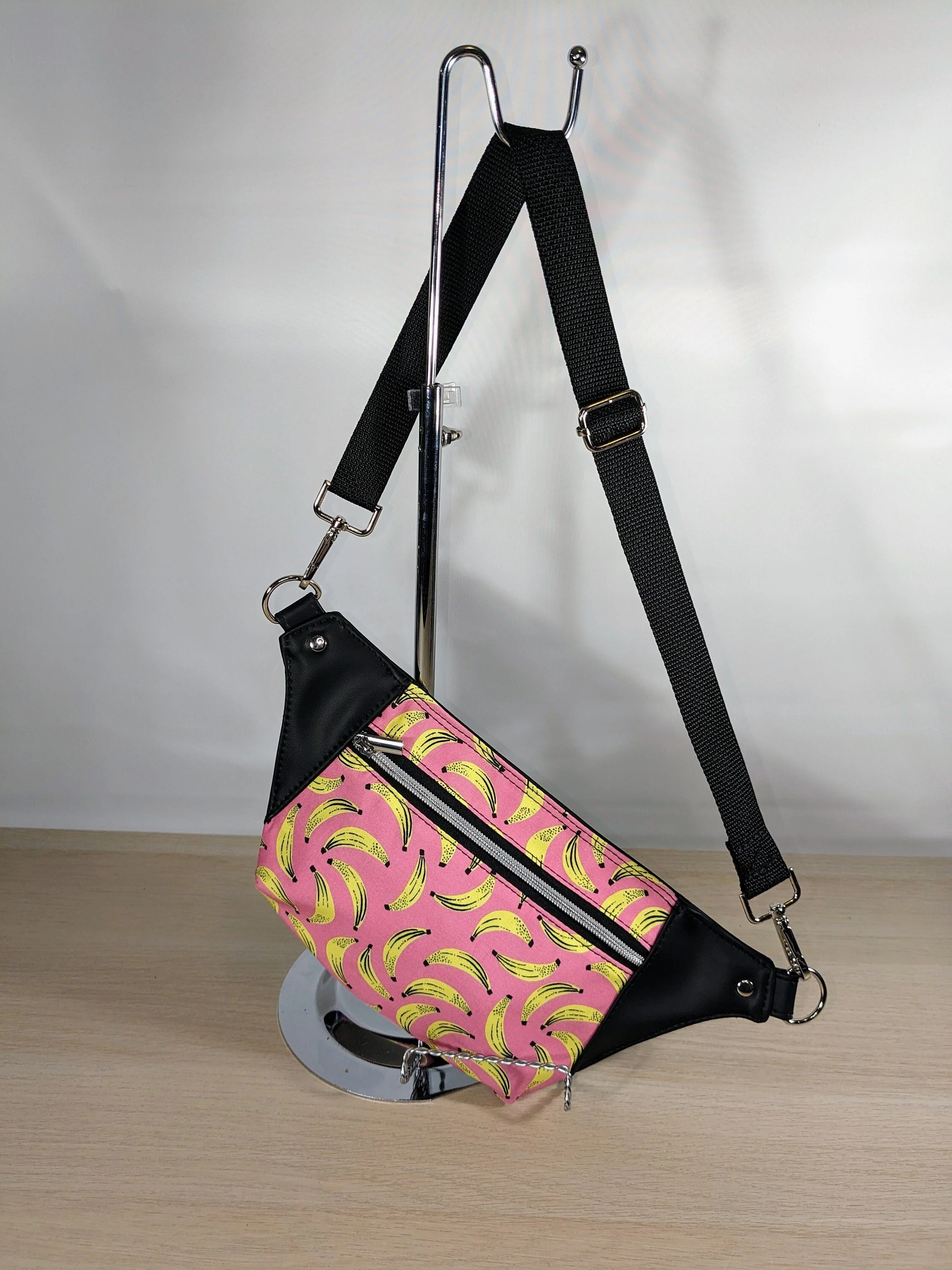 A pink and yellow banana-patterned bag hanging on a mannequin stand with a black strap.