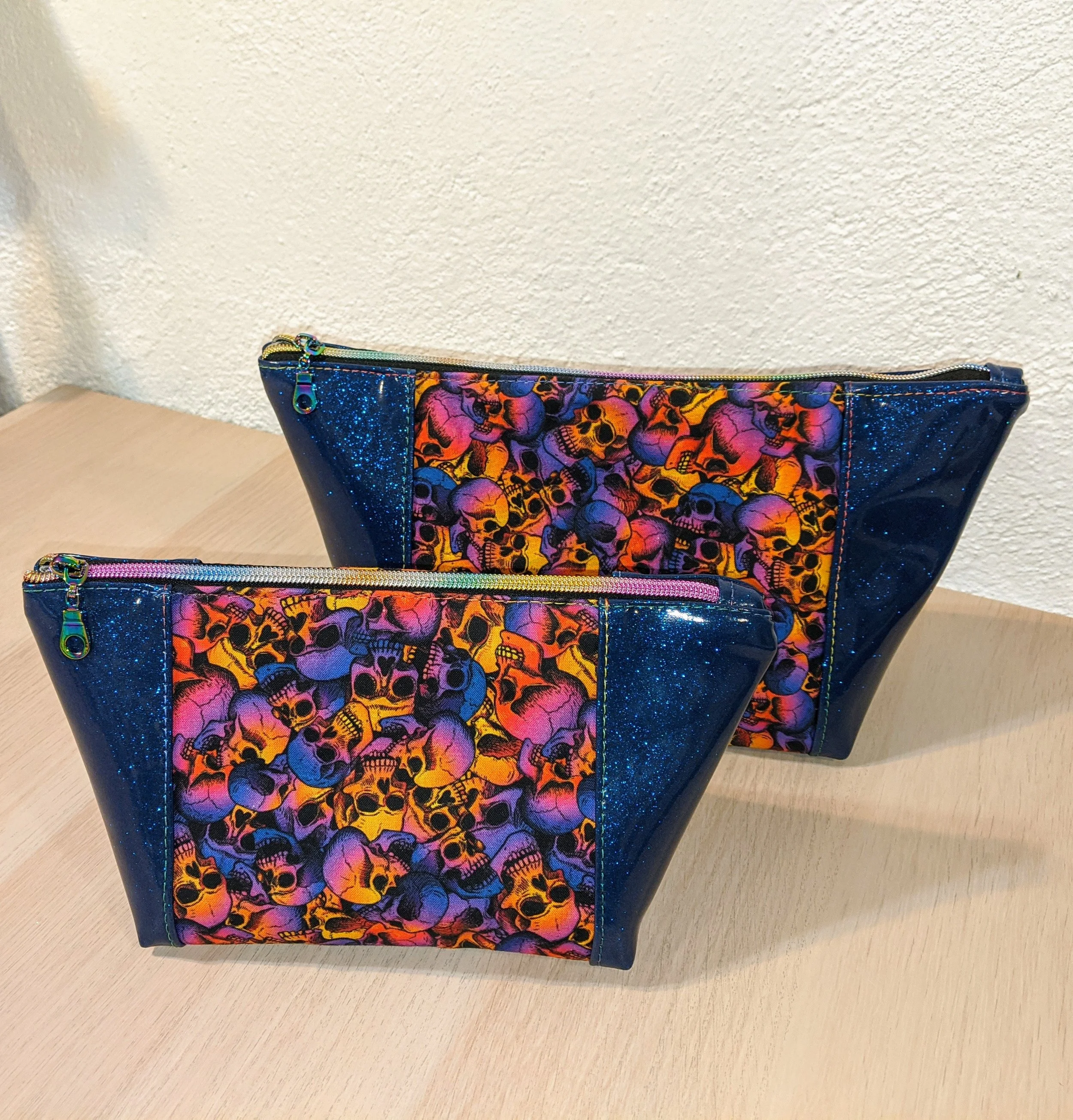 Two colorful bags with skull designs and blue glitter accents on a light wooden surface.