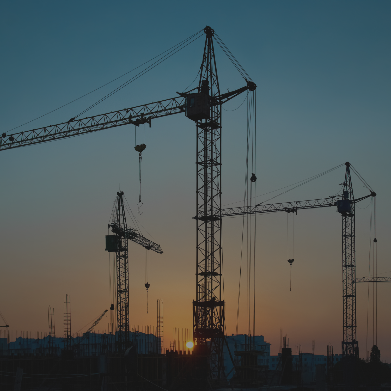 Construction site with several tower cranes at sunset.