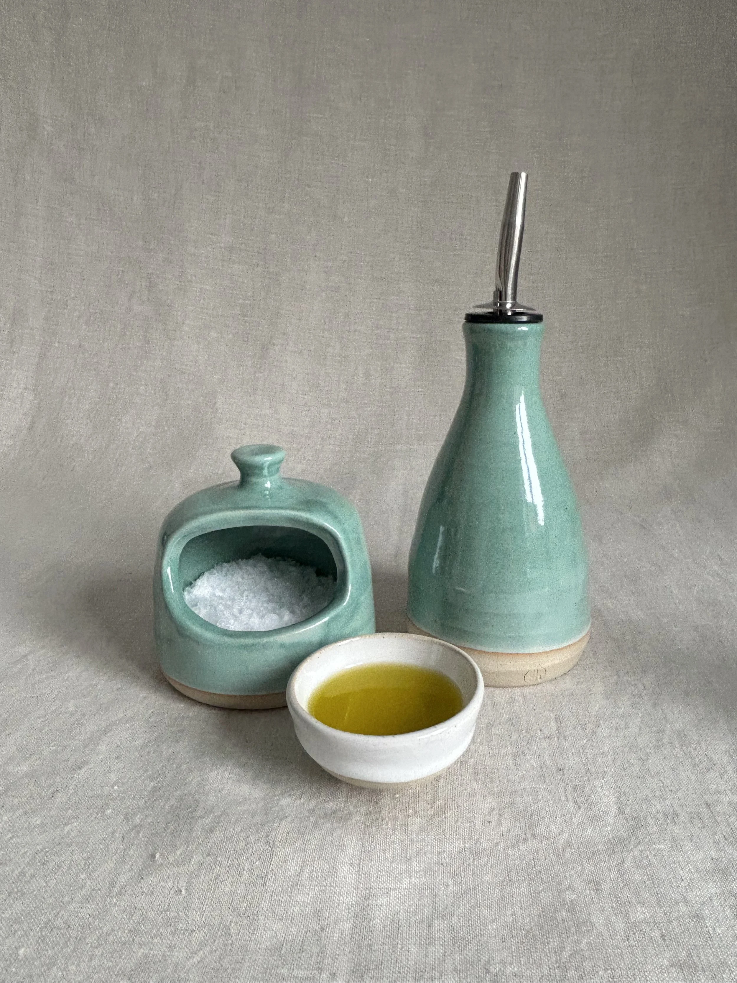 Ceramic tableware set with two turquoise vases, one filled with salt, the other with olive oil, against a plain beige background.