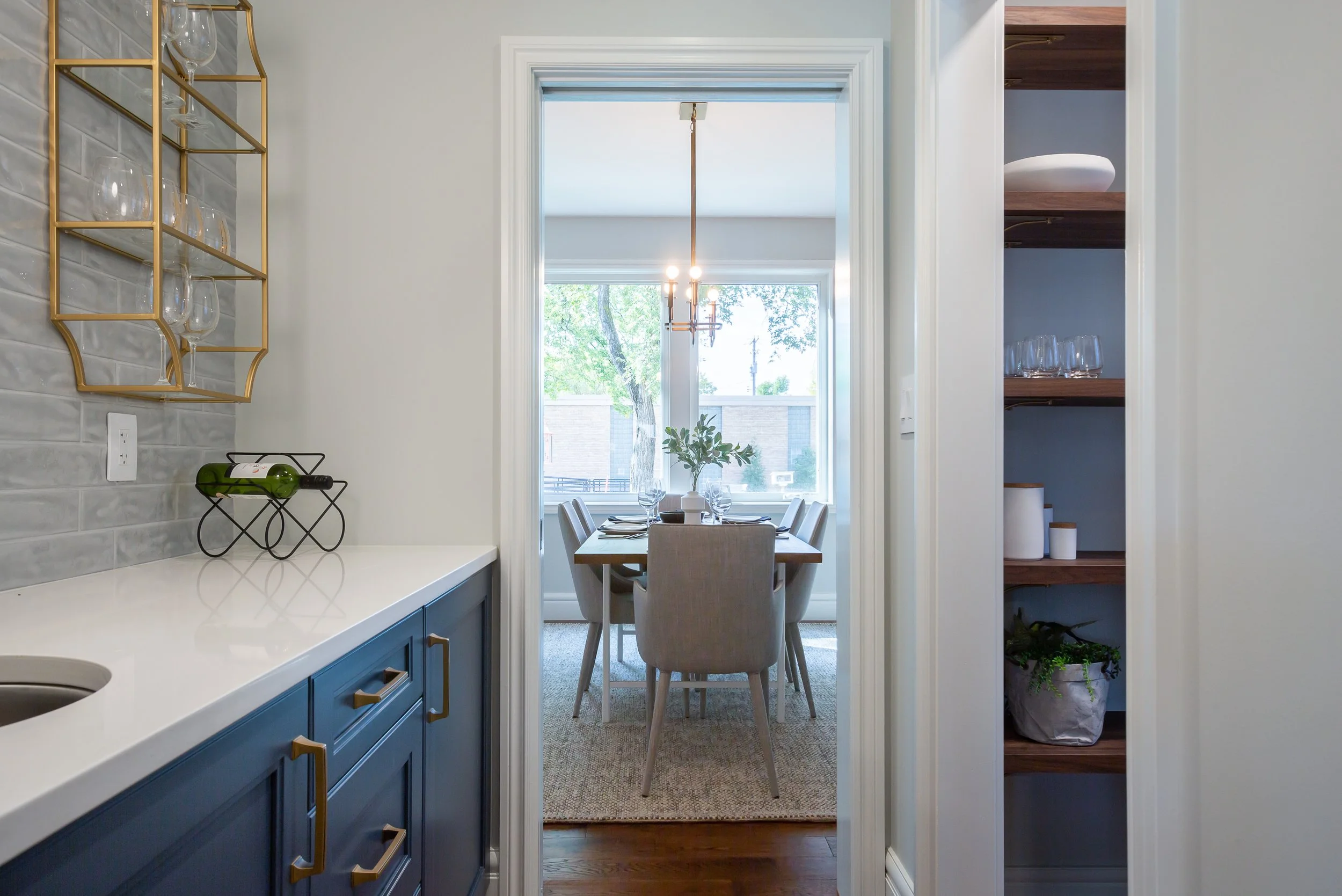 View through doorway into a dining room with a table set for four, large window, and a modern chandelier