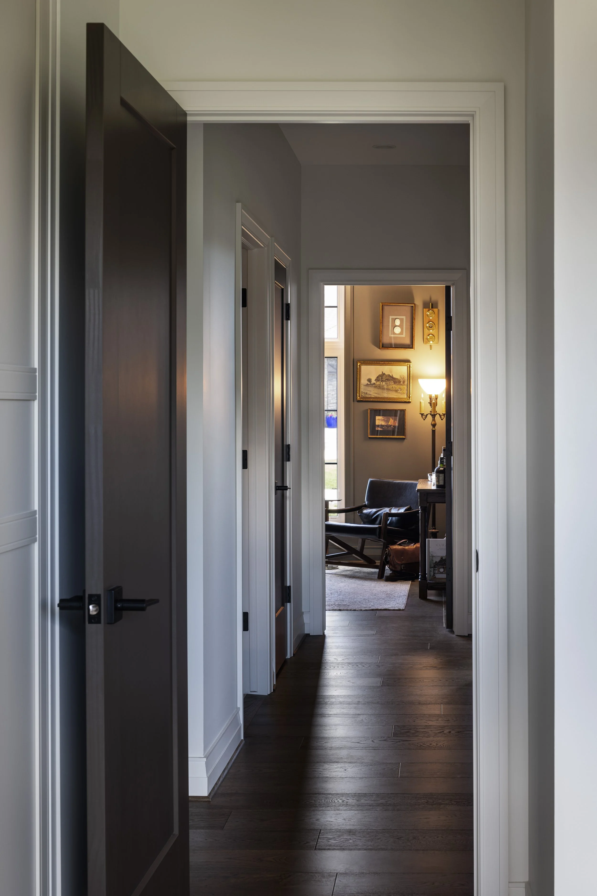 View of an interior hallway leading to a sitting area with framed pictures, a floor lamp, chair, and window.