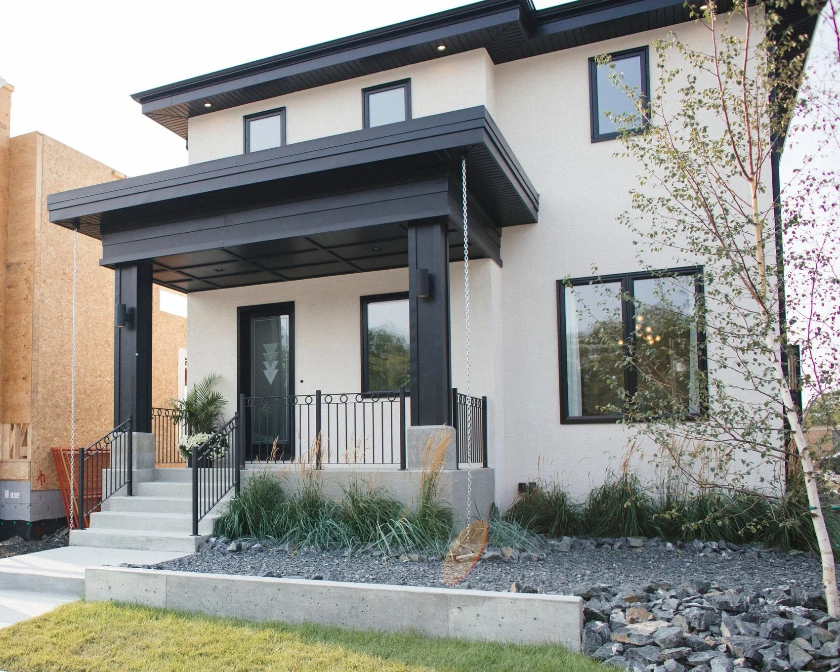 Modern two-story house with a black covered porch, front steps, and landscaped yard with rocks and grass.