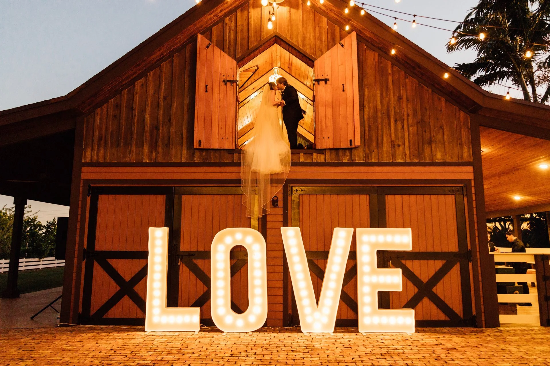 Wedding couple kissing above rustic barn with large "LOVE" sign.