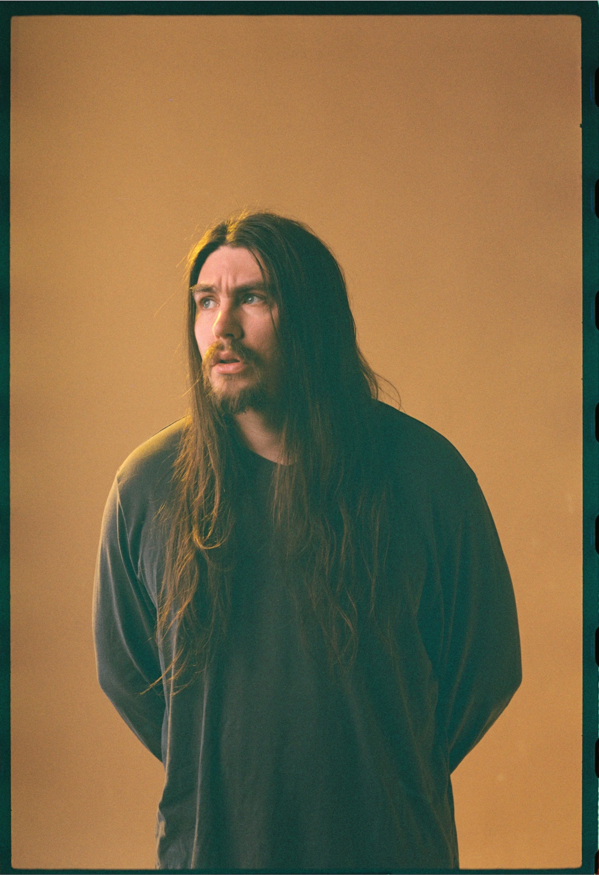 A film photograph of a long haired man staring past the camera