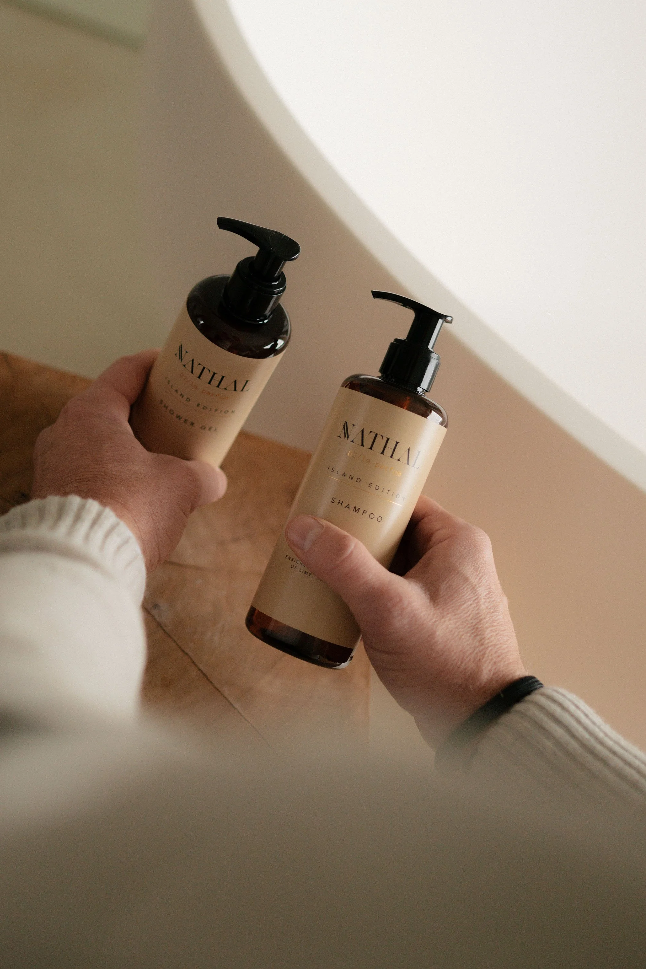 A person holding bottles of Nathal Island Edition shampoo and shower gel on a wooden surface.