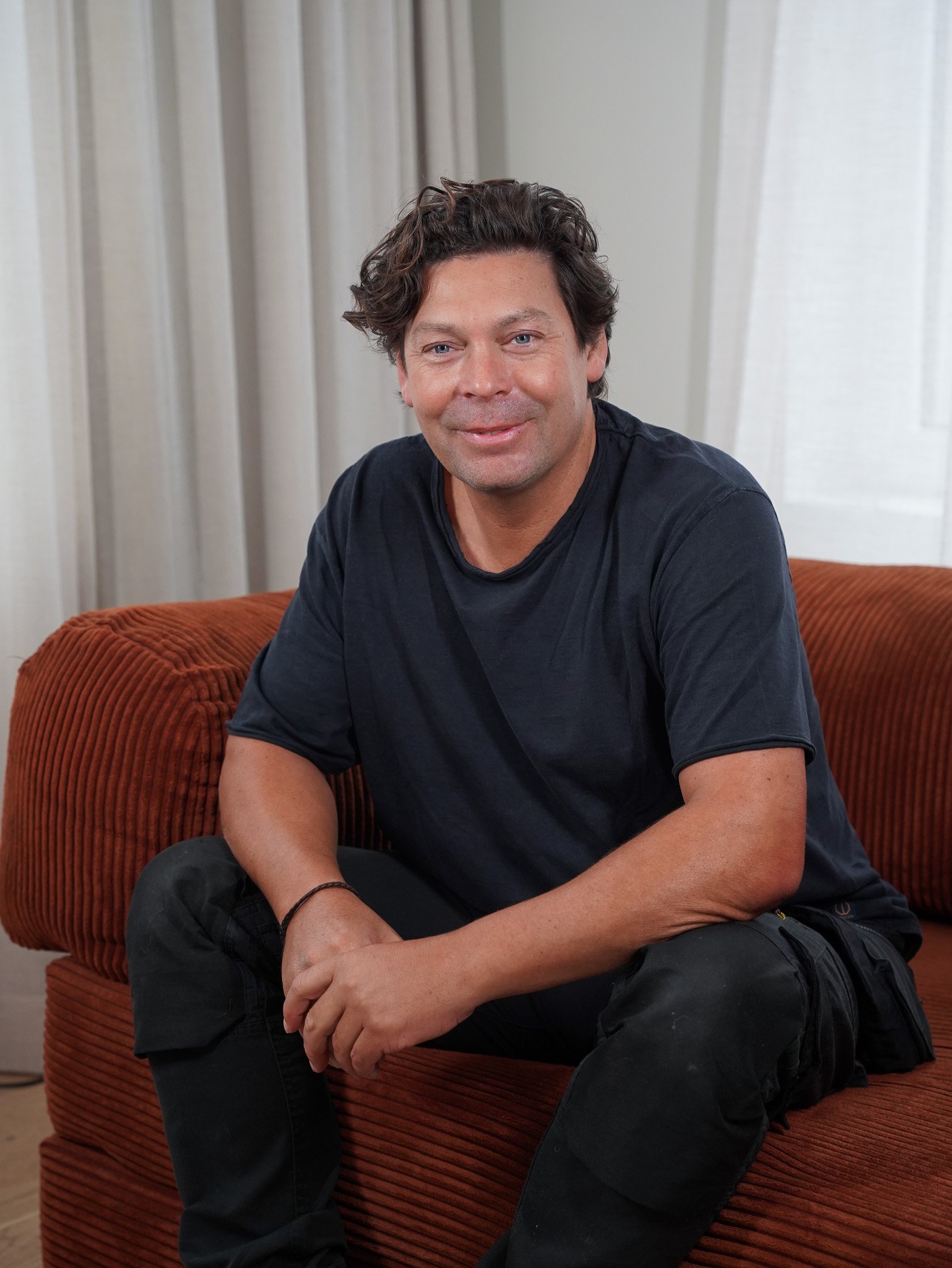 Man wearing glasses and a green sweater looking to the side, with a blurred background.
