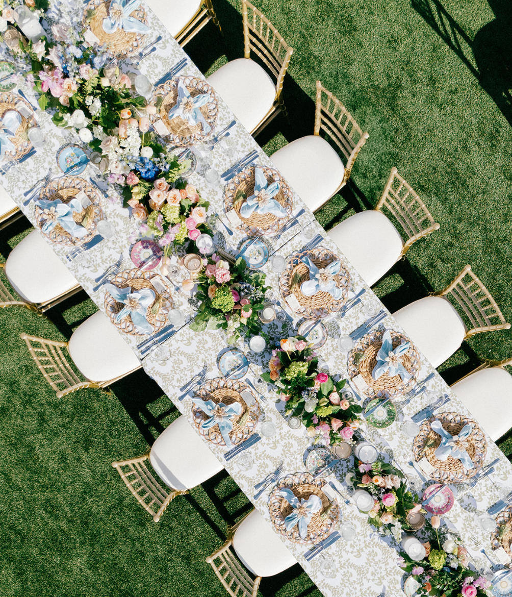Overhead view of a long outdoor banquet table decorated with floral arrangements and place settings.