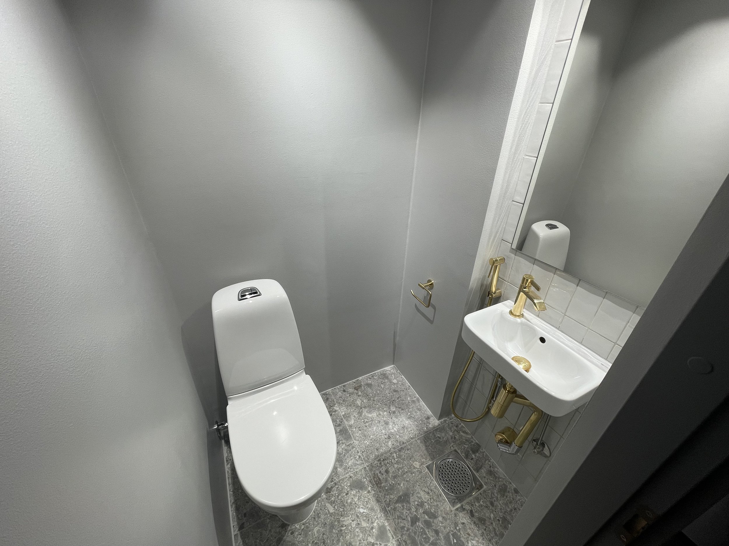 Pieni wc-tila, jossa on valkoinen WC-istuin, pieni valkoinen allas ja kultaiset hanat, peili ja seinät.