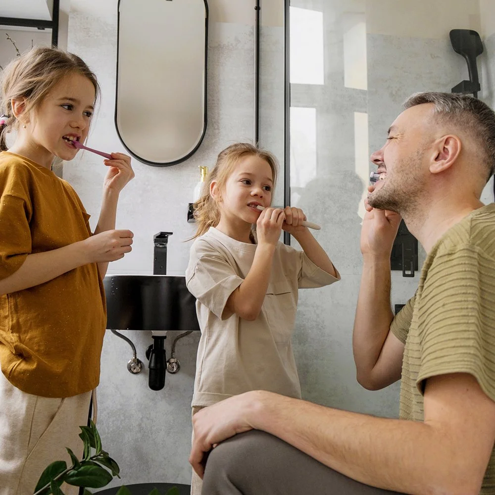 A father and his two daugthers brushing their teeth in a bathroom