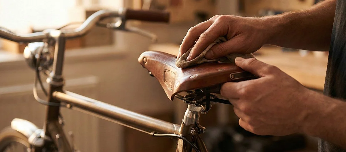 Två händer som vårdar en gammal cykelsadel i läder