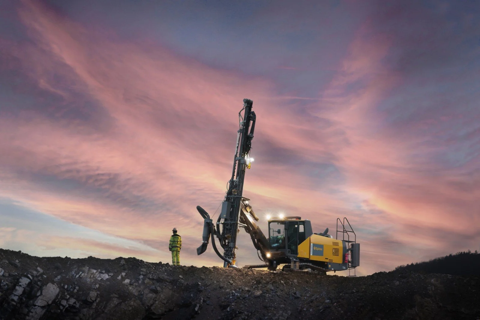 A man standing beside a rock drill in sunset