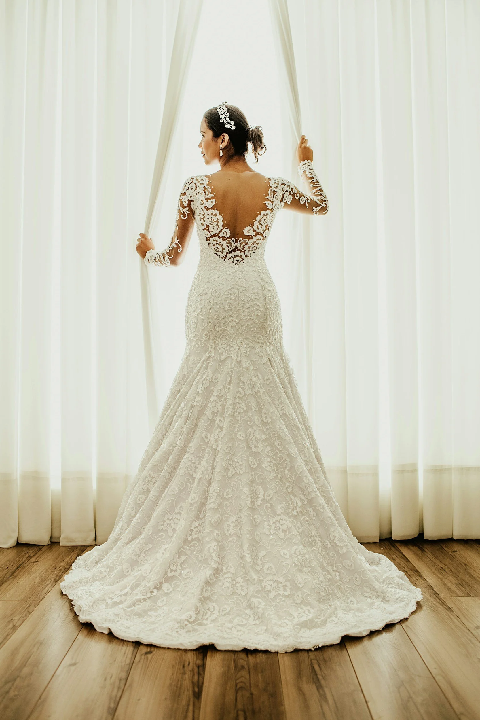Bride in lace wedding dress standing in front of white curtains