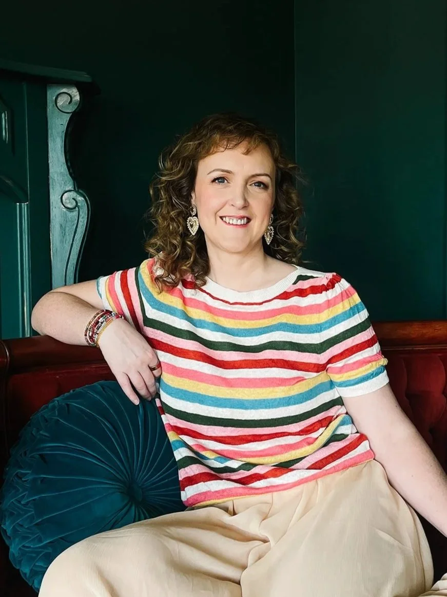 moyra-sitting-rainbow-top-smiling-at-camera.jpg