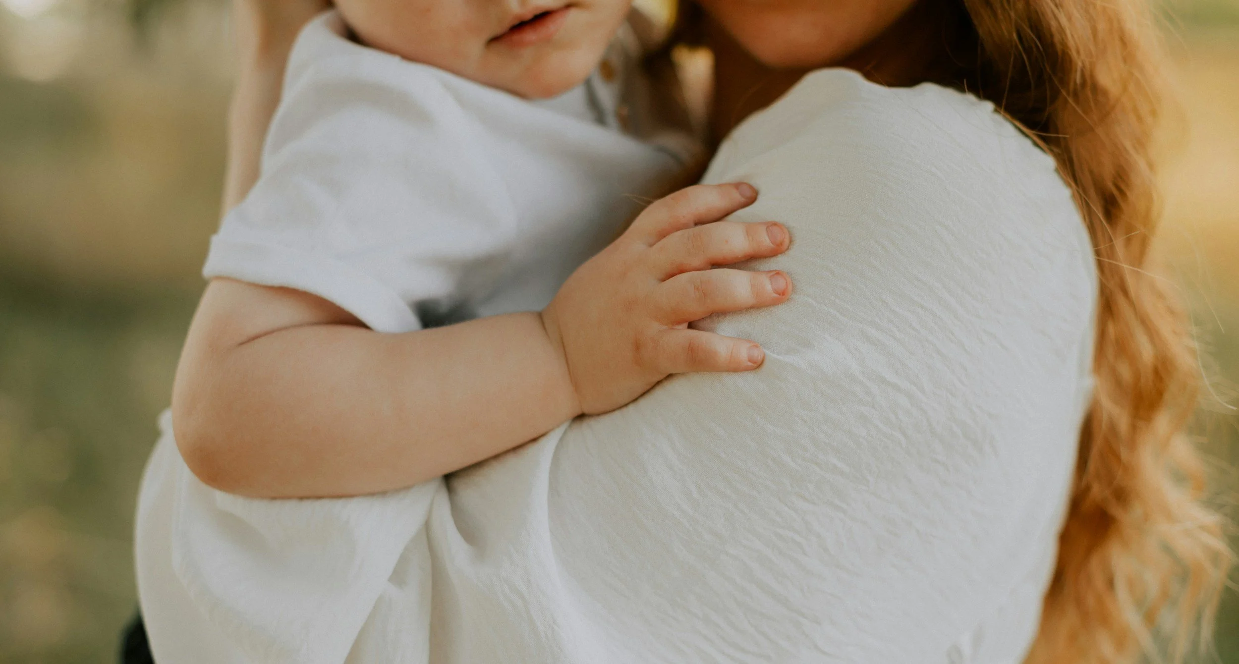 Close-up of a small child's hand resting on an adult's shoulder, with the child wearing a white shirt and having curly hair.