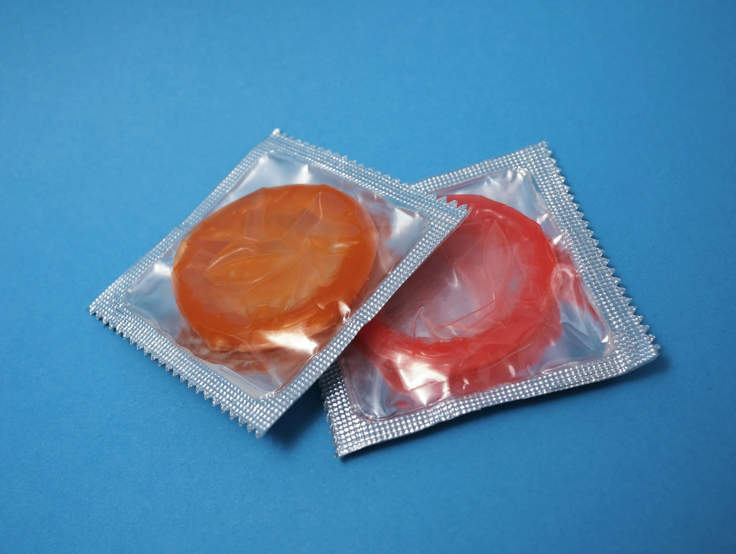 Two packaged condoms, one orange and one red, on a blue surface.