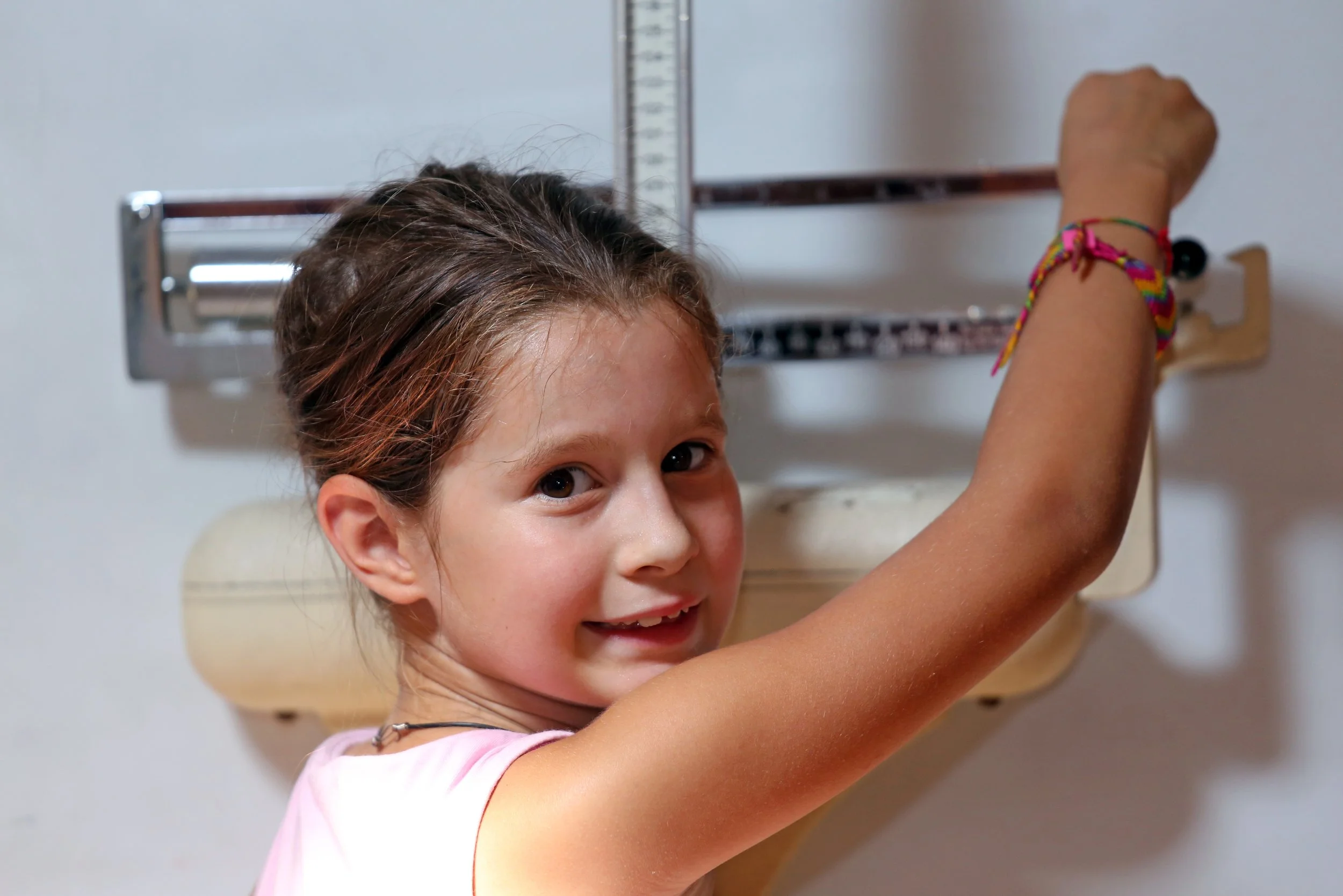 A young girl with brown hair and wearing a pink shirt is smiling while drawing on a whiteboard.
