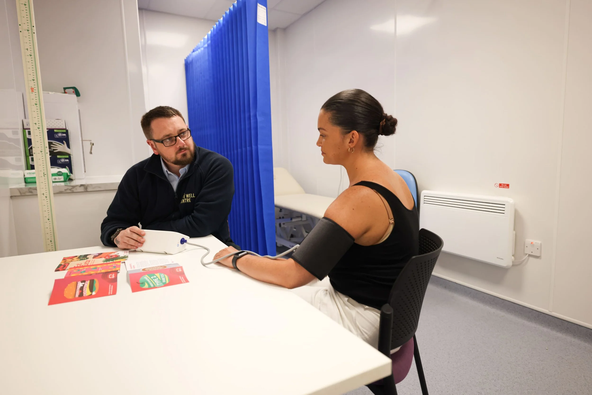 A woman having her blood pressure taken by a healthcare professional in a clinic setting.