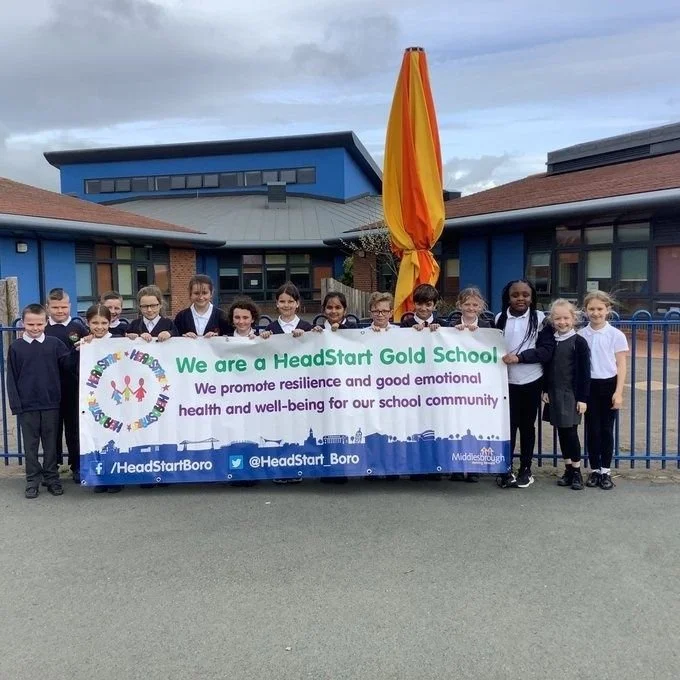 Group of school children holding a banner outside a school building, promoting resilience and emotional well-being.