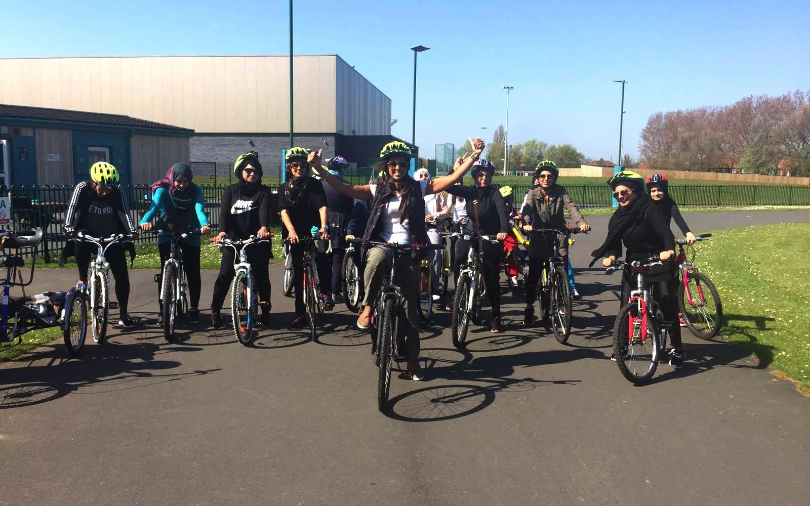 Group of women with helmets on bikes at a park on a sunny day.