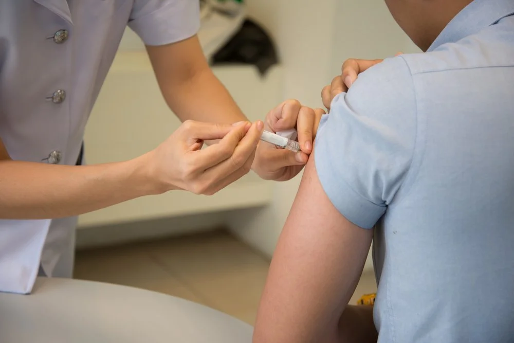 A healthcare professional administering a vaccine injection into a person's arm in a clinical setting.