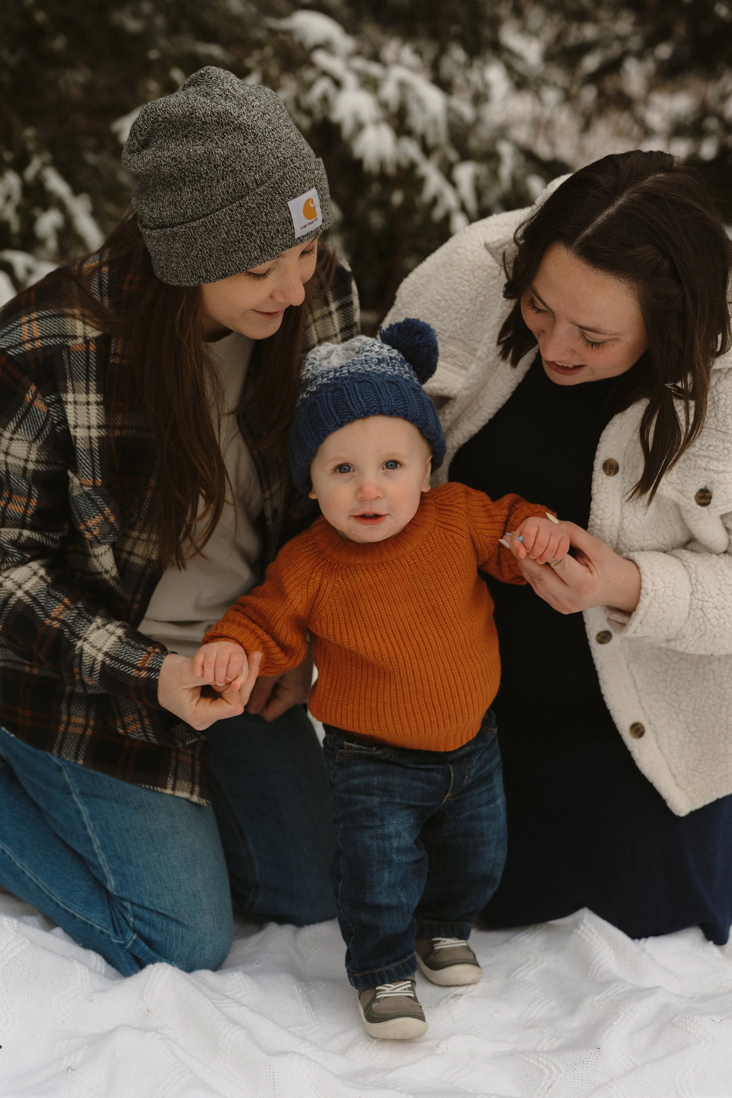 Sweet little boy holding his parents hands in the snow.
