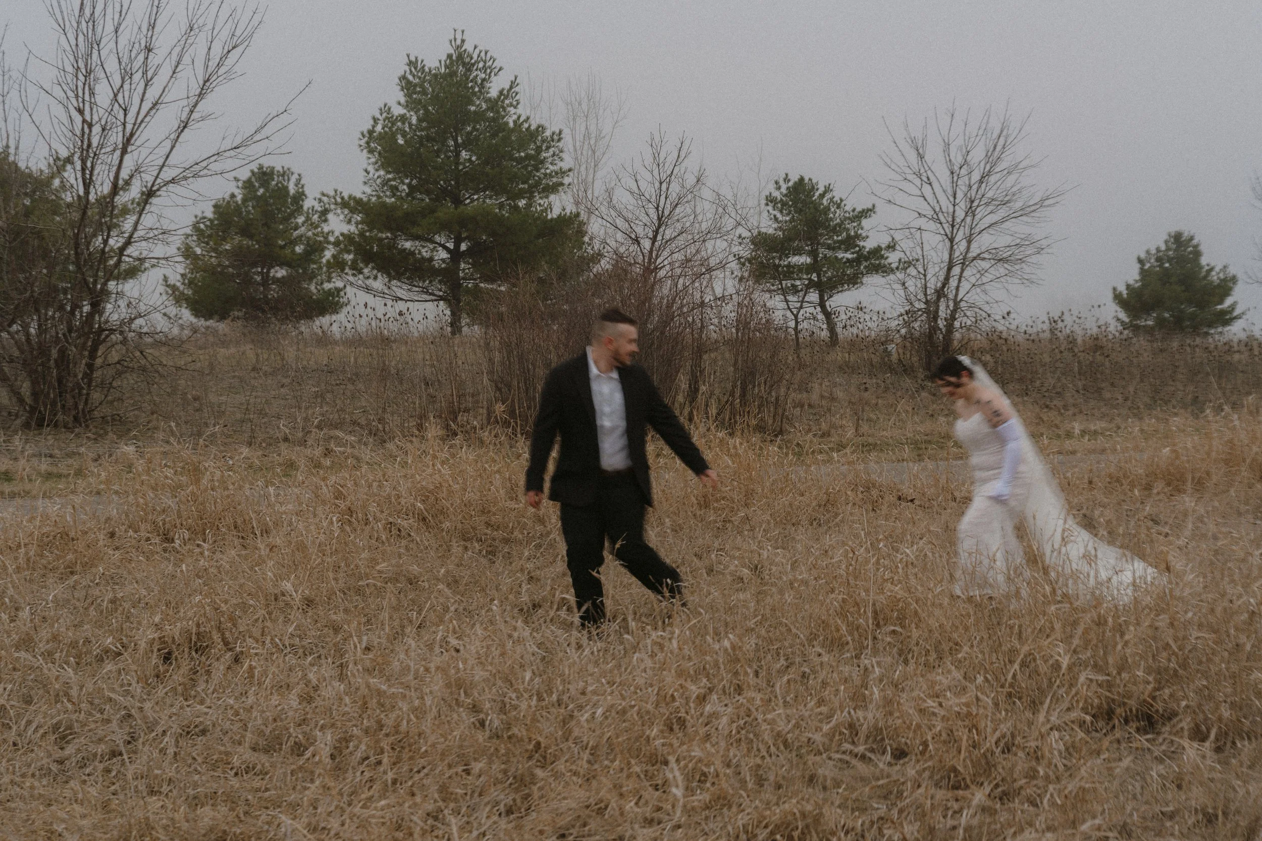 Groom and Bride running through a field in winter together.