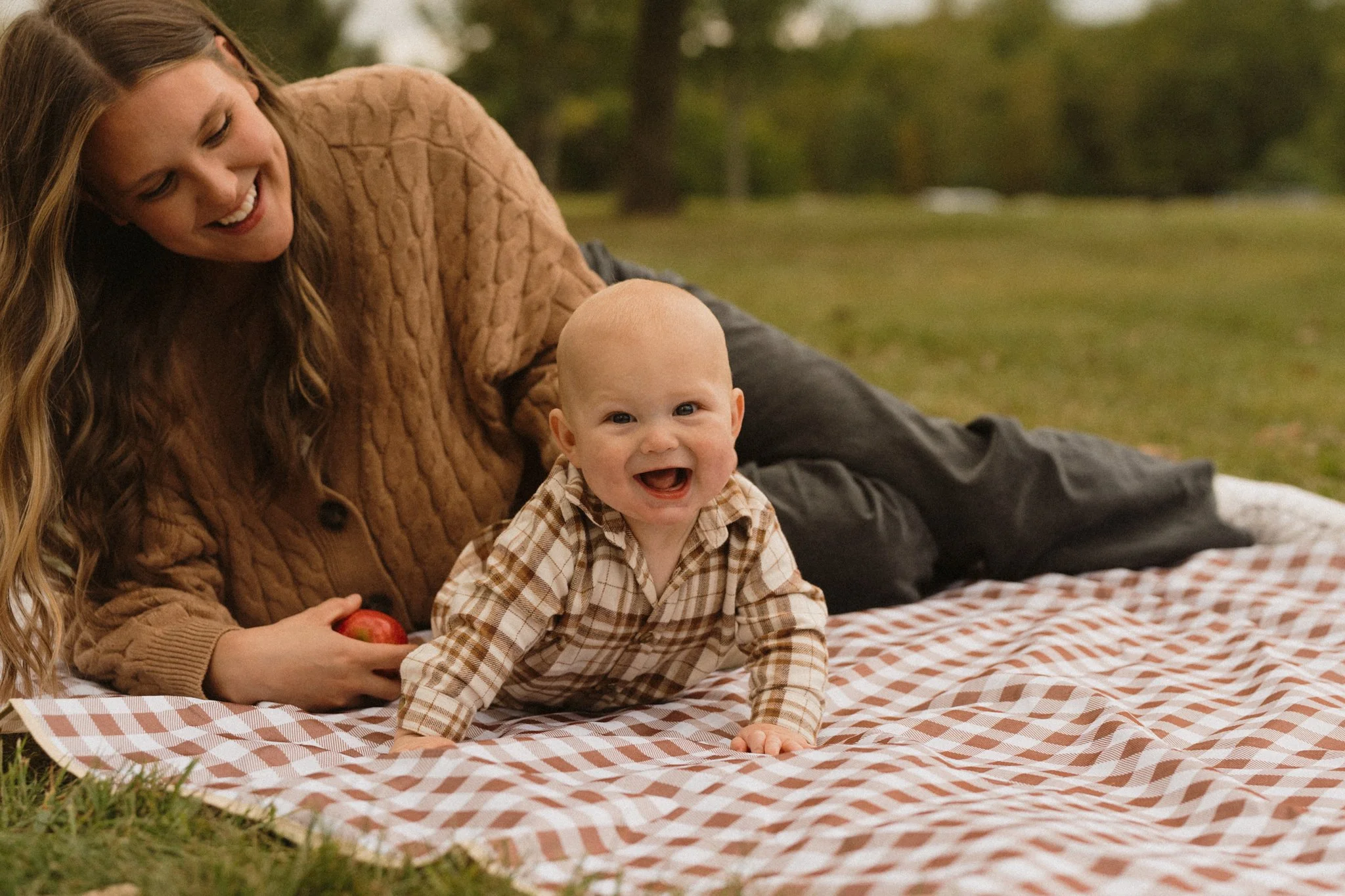 A mother and baby on a picnic blanket.