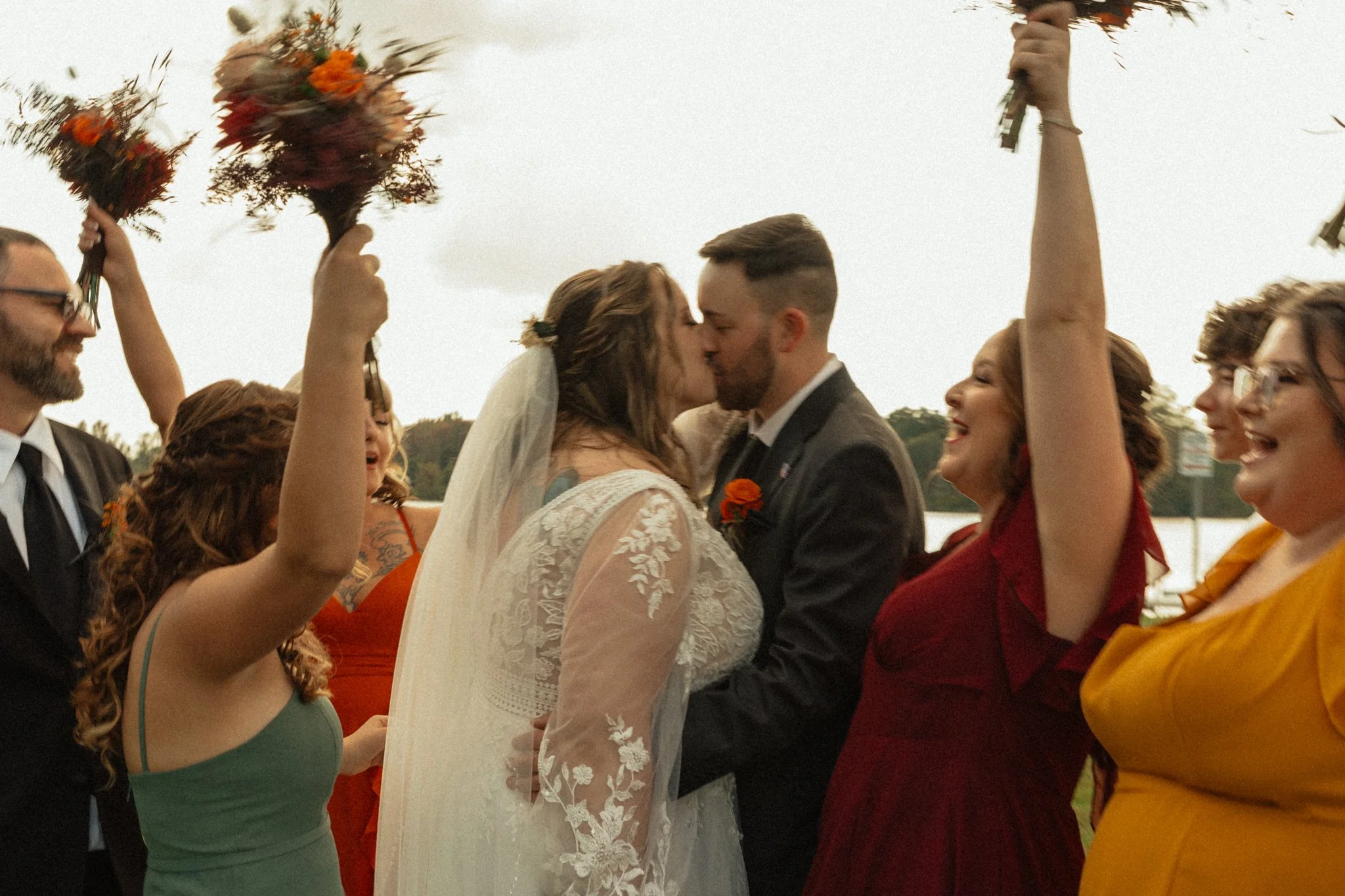 Newly married couple kissing while wedding party celebrate.