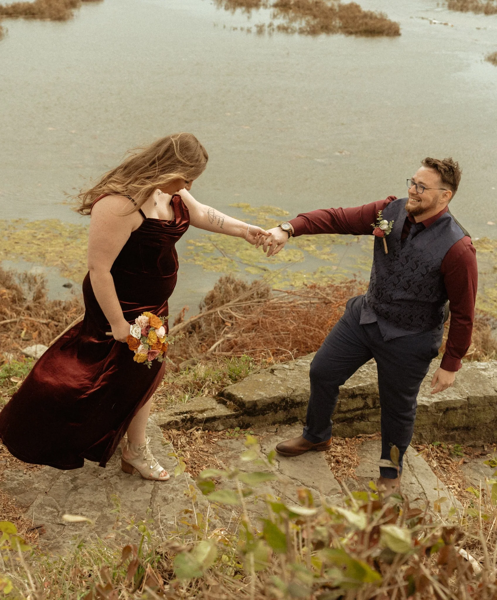 Bride and groom walking down rock staircase along a river.