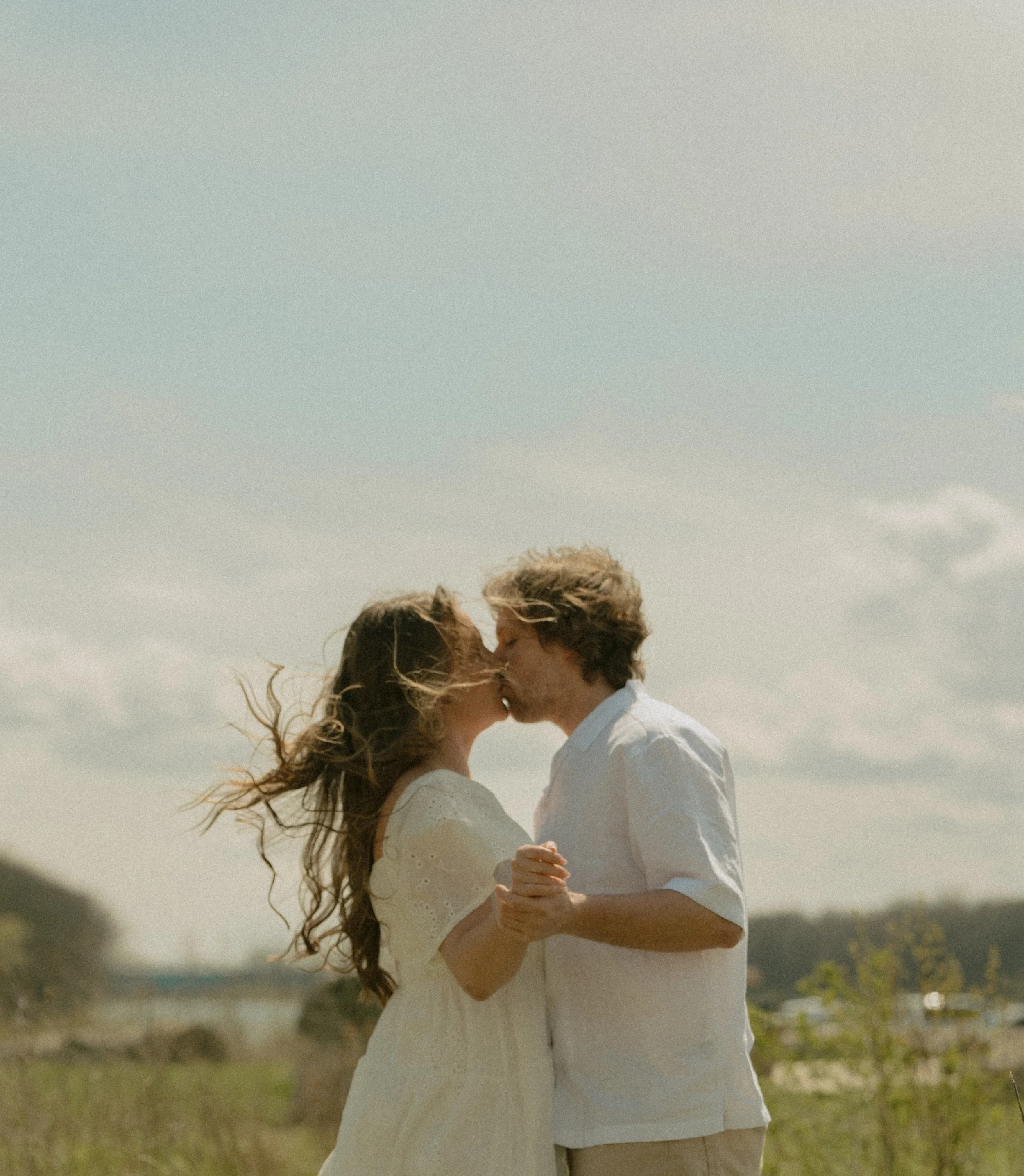 Couple kissing in front of a beautiful cloud filled sky