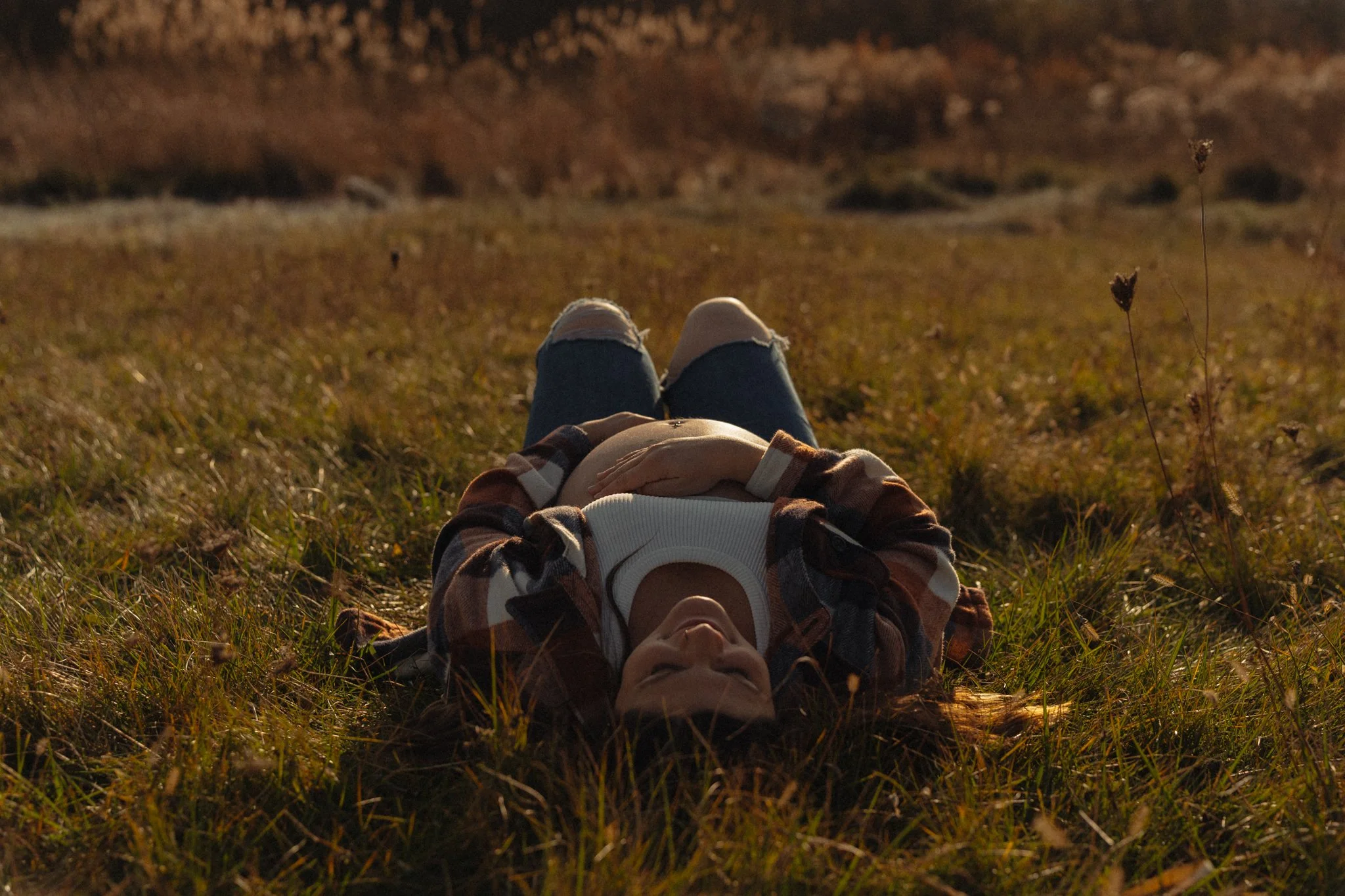 Pregnant mama laying on her back in a field at golden hour with her belly out in the sun.