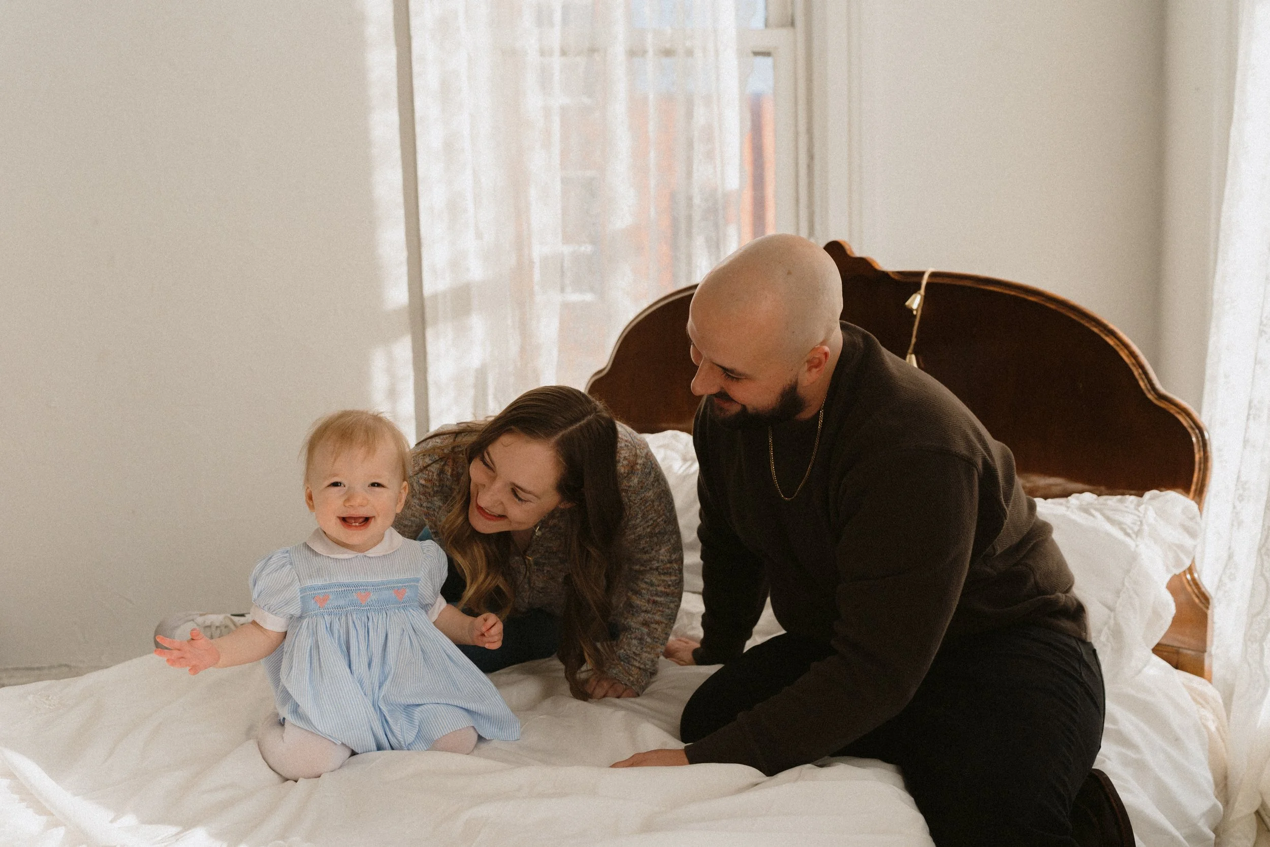 Family sitting on a bed in a photo studio. Baby girl is smiling hugely.