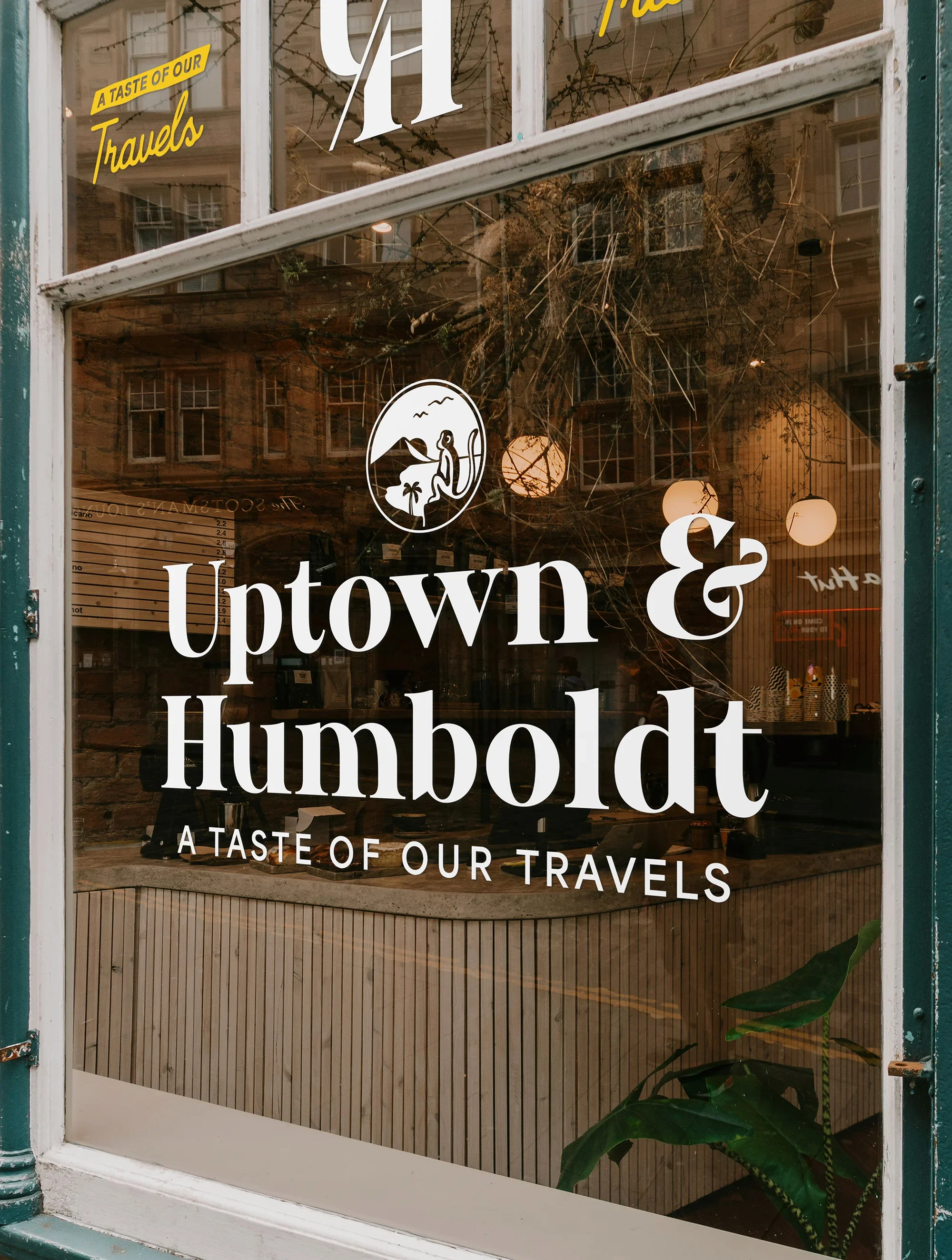 Close-up of a sandwich with lettuce, coleslaw, and fried chicken on a bun, placed on a black plate, with a green and yellow Uptown & Humboldt logo overlay in the center.