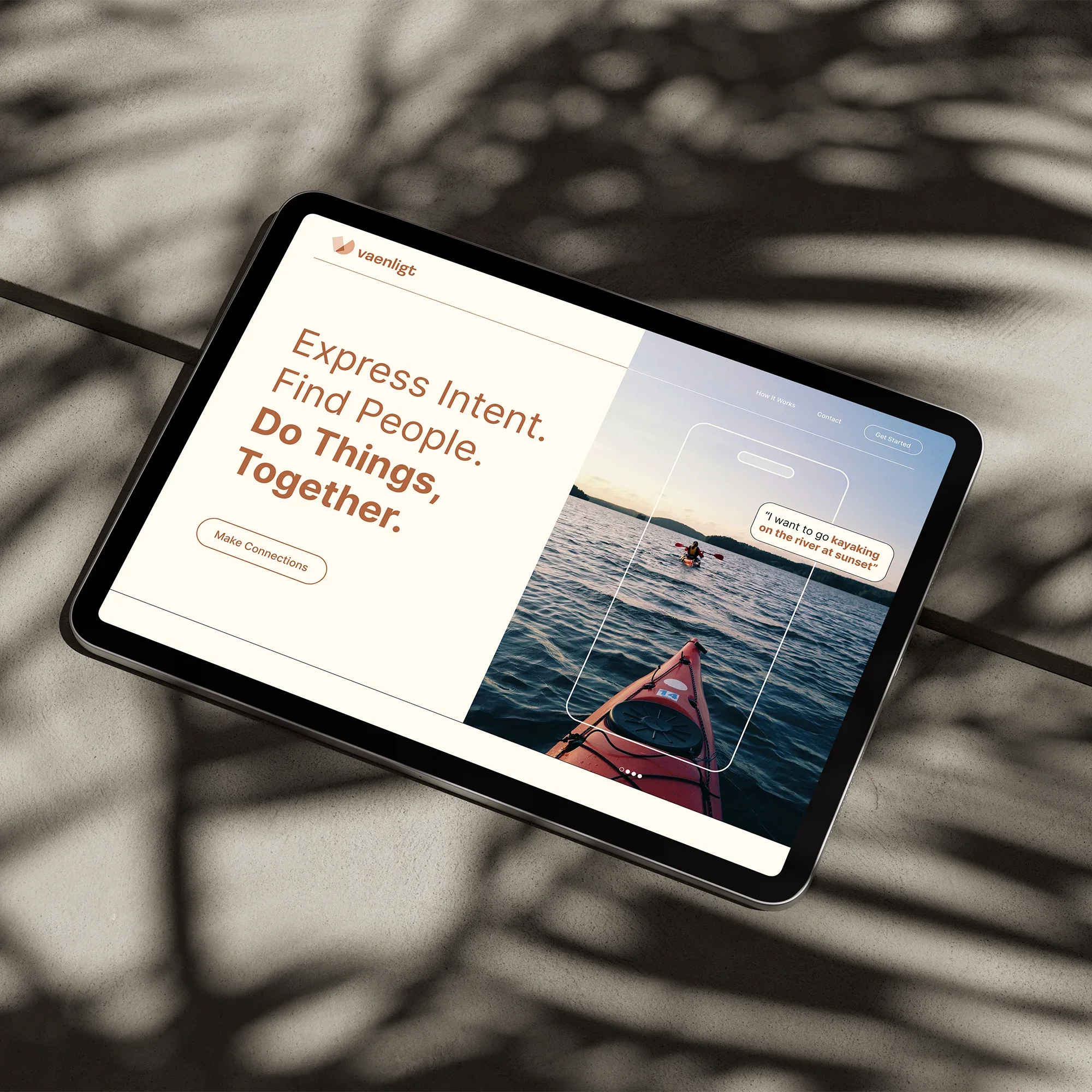 Tablet displaying a website with a kayak on a lake and the text "Express Intent. Find People. Do Things, Together." on a beach with shadows of leaves.