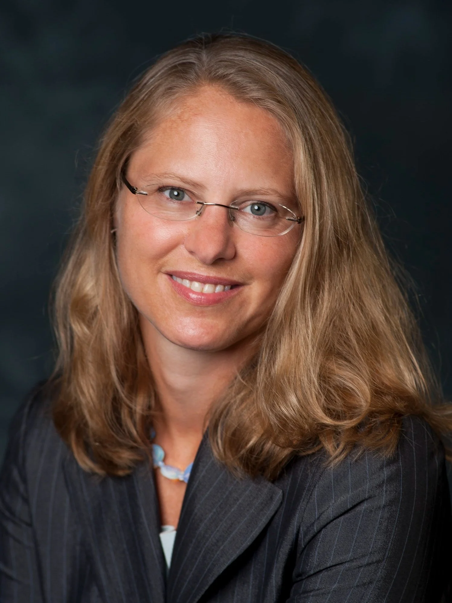 Professional portrait of Maya Gasuk from West Wind Consulting. She is smiling and has shoulder-length light brown hair, glasses is wearing a blazer.