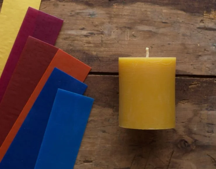 Colorful candles in pink, purple, orange, blue, and yellow arranged on a wooden surface, with a single yellow candle standing upright.
