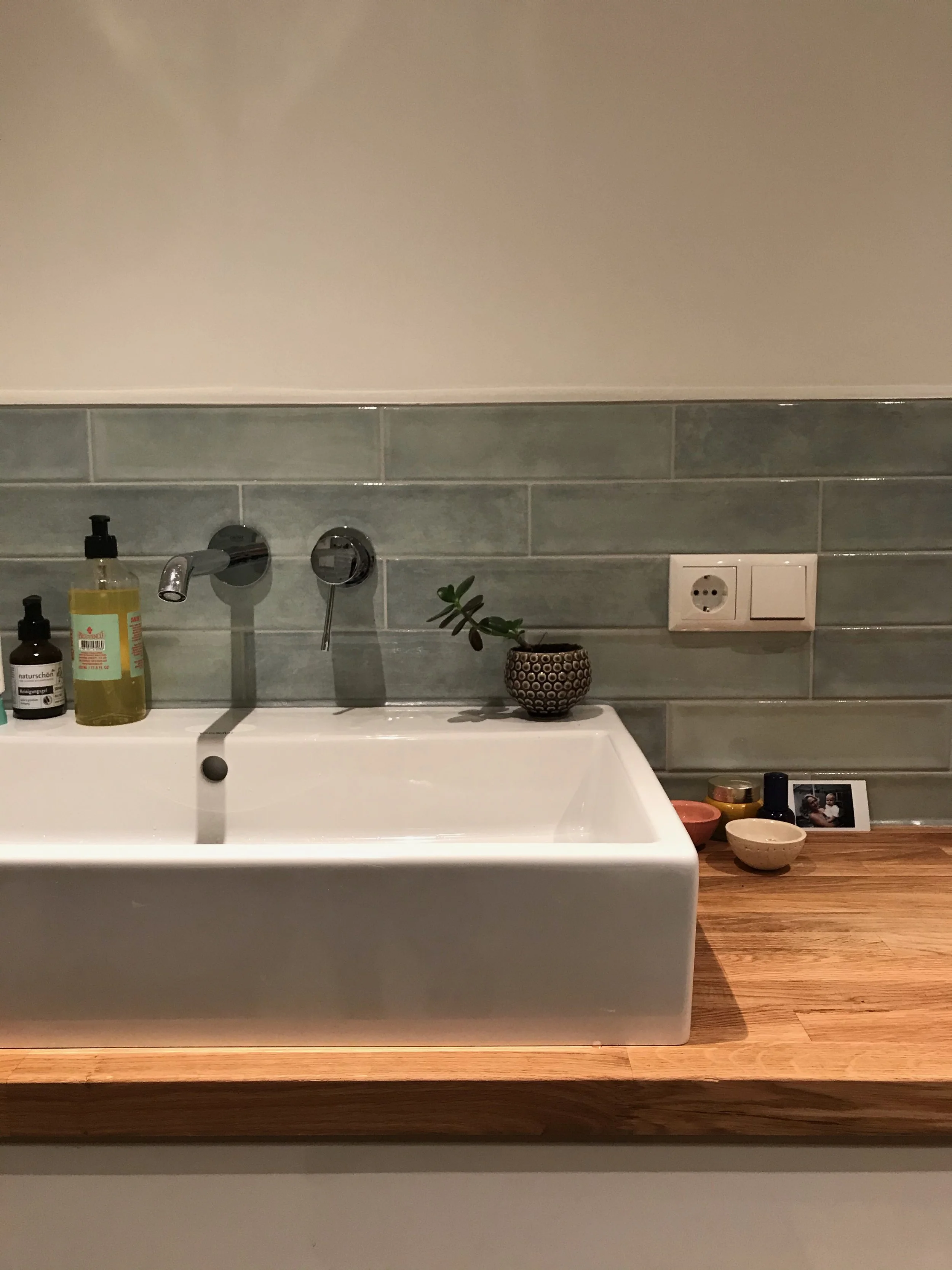 Badezimmer, grüne Fliesen, Waschbecken, kleine Pflanze