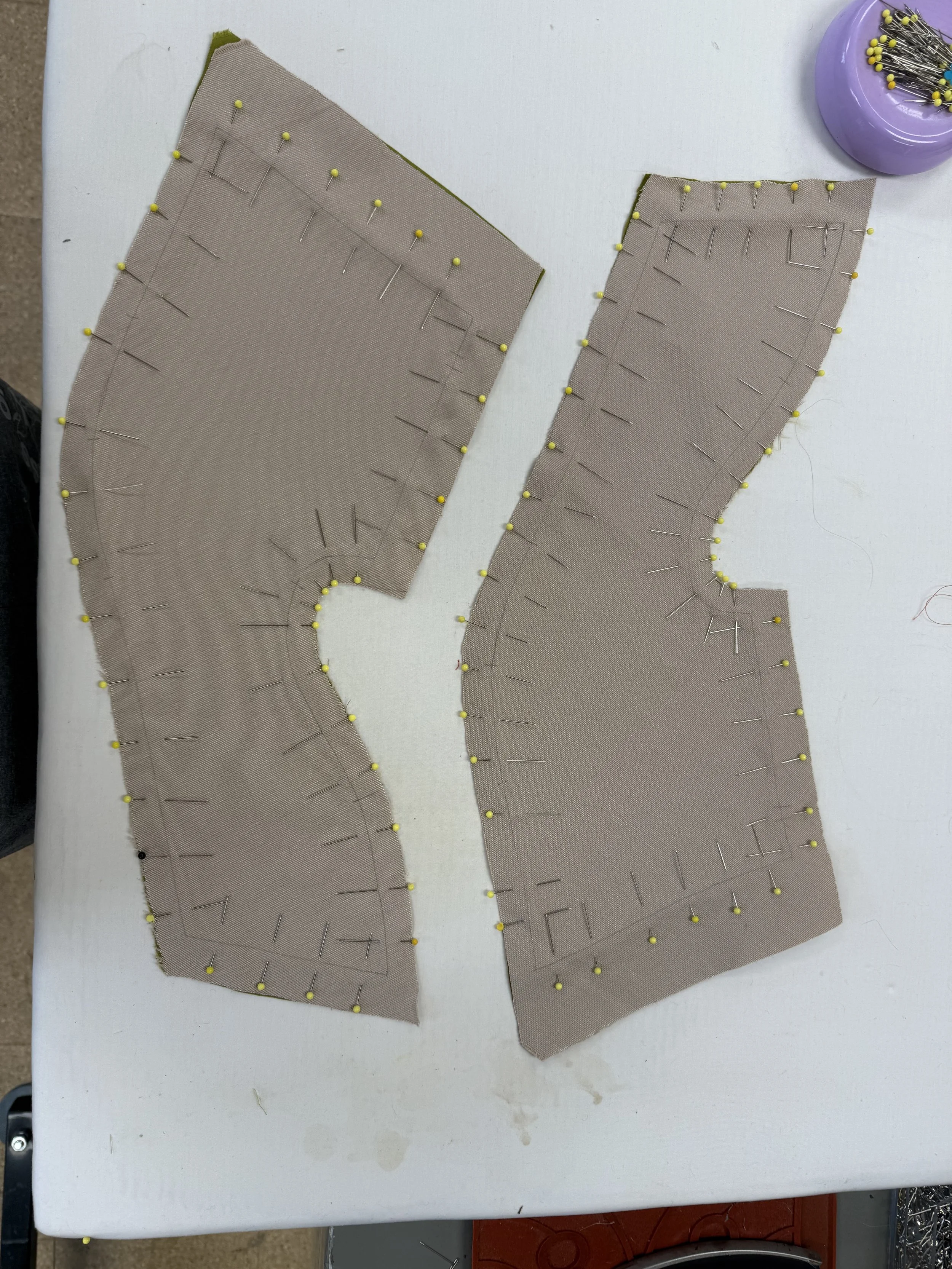 Two pieces of fabric with pins and markings, likely pattern pieces for sewing, on a white work surface.