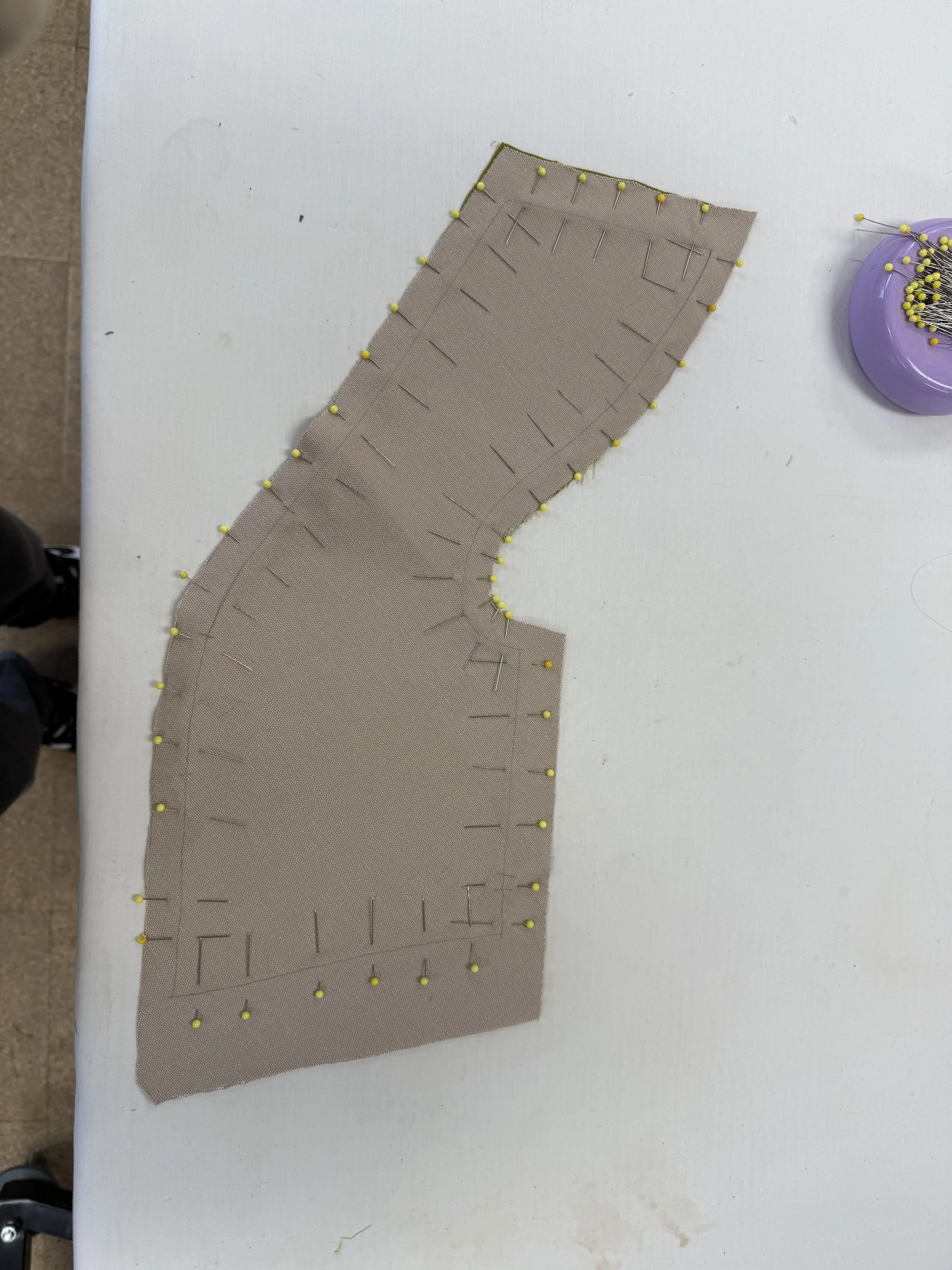 Fabric pattern with pinned fabric pieces on a white table, likely part of a sewing or tailoring project.