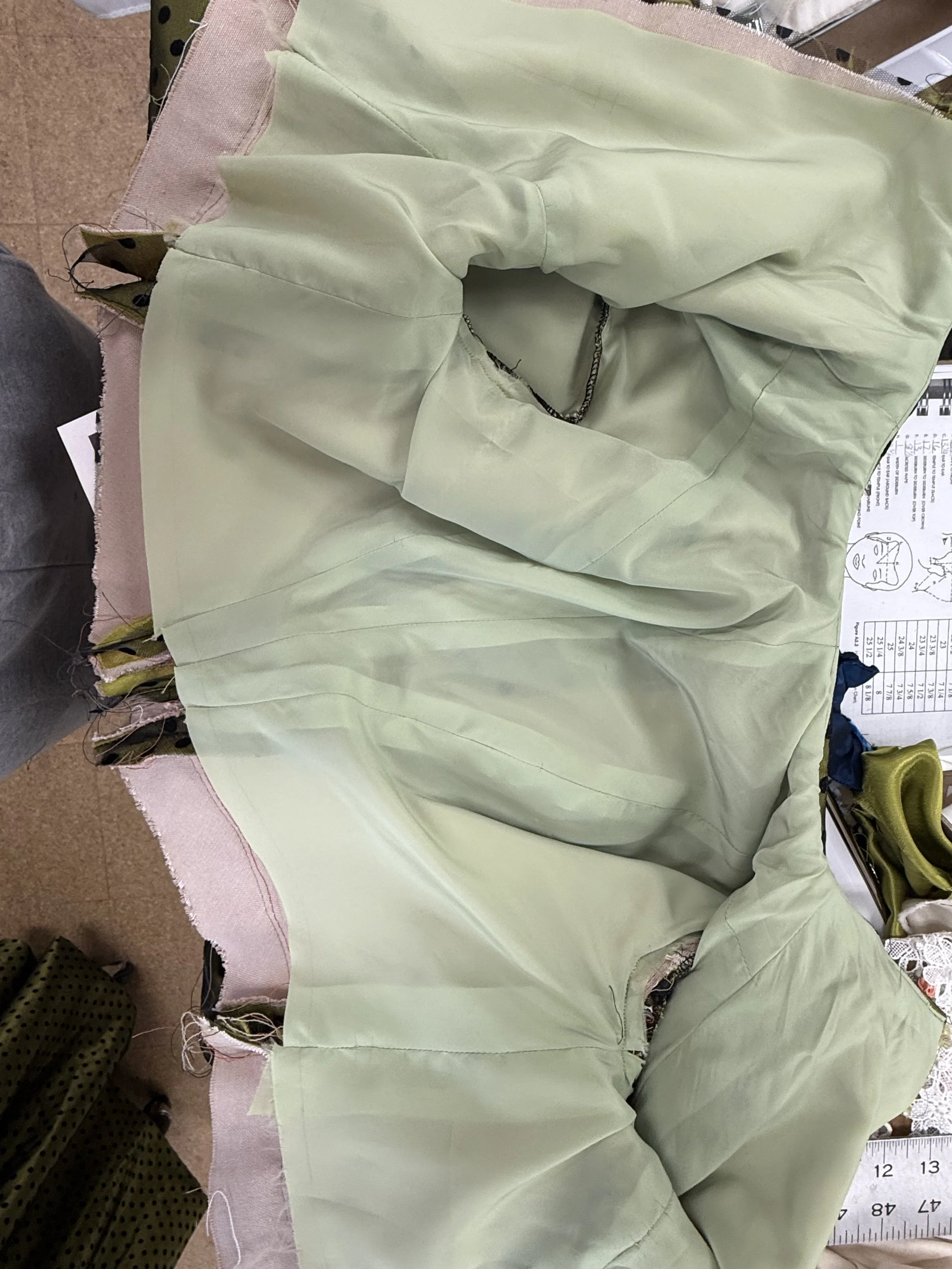 Light green fabric or garment laid out on a surface, partially sewn with visible seams and frayed edges.
