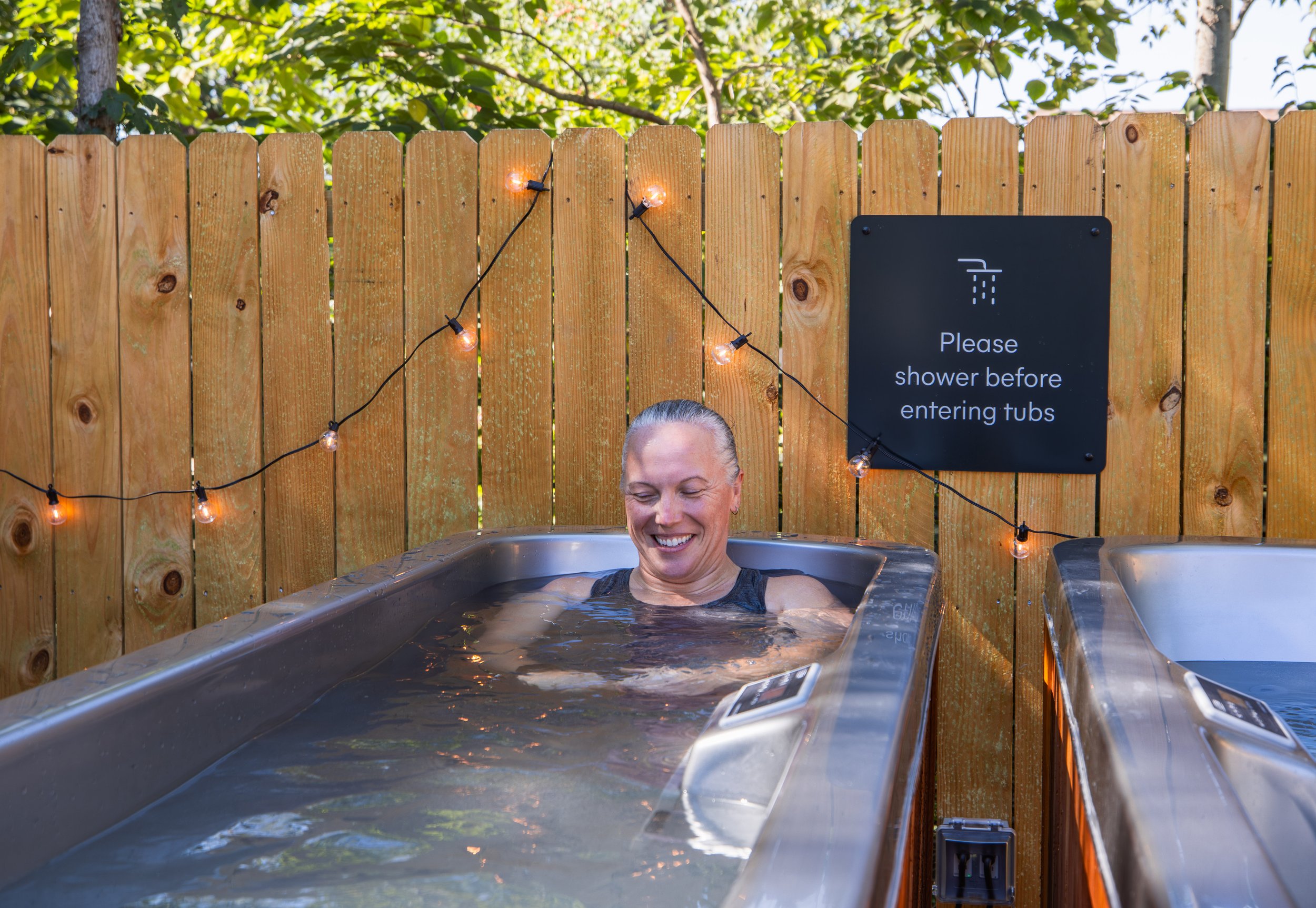 Woman smiling in cold tub in Framework backyard space next to a fence with lights.