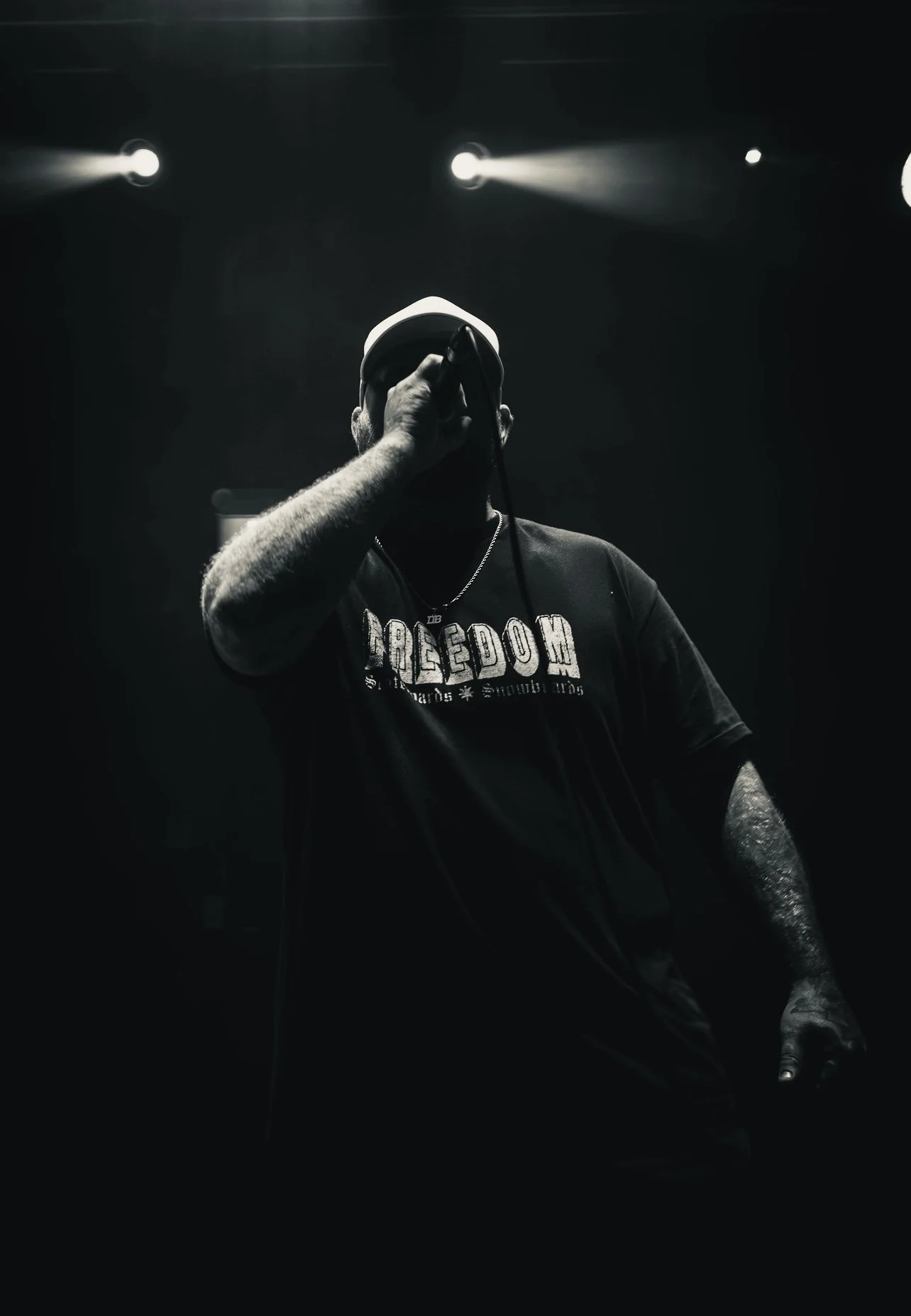 A person performing on stage in a dark environment, holding a microphone close to their mouth, illuminated by stage lights.