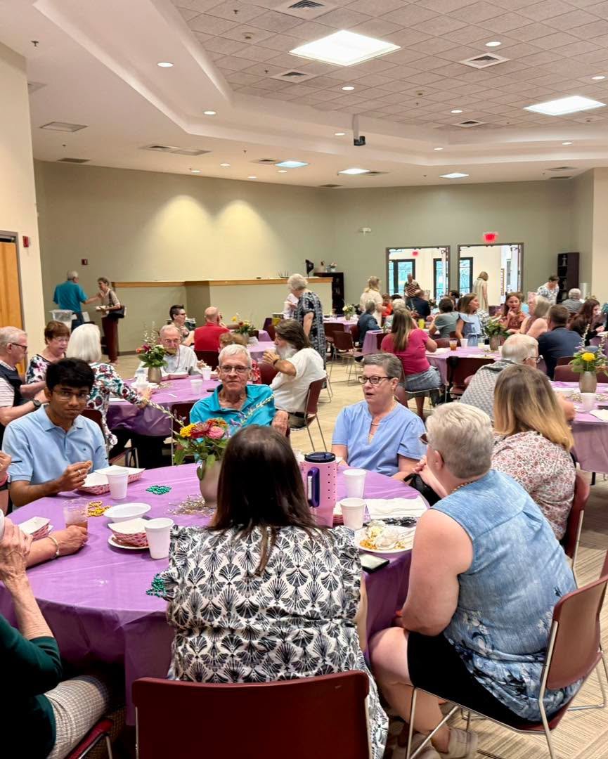 People sitting around decorated tables at an indoor event hall during a gathering or celebration.