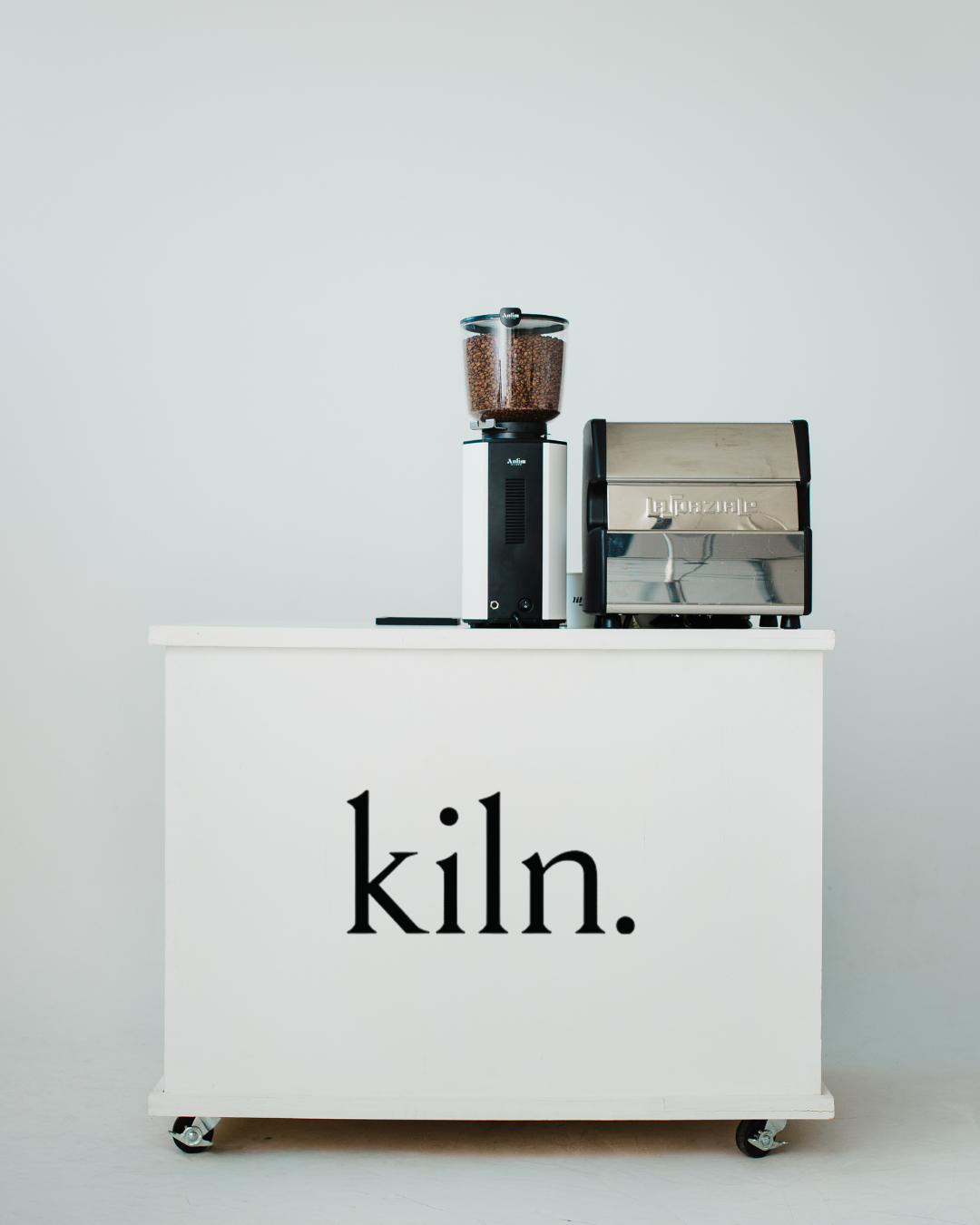 Coffee grinder and espresso machine on a white cart with the word 'kln.' printed on it.