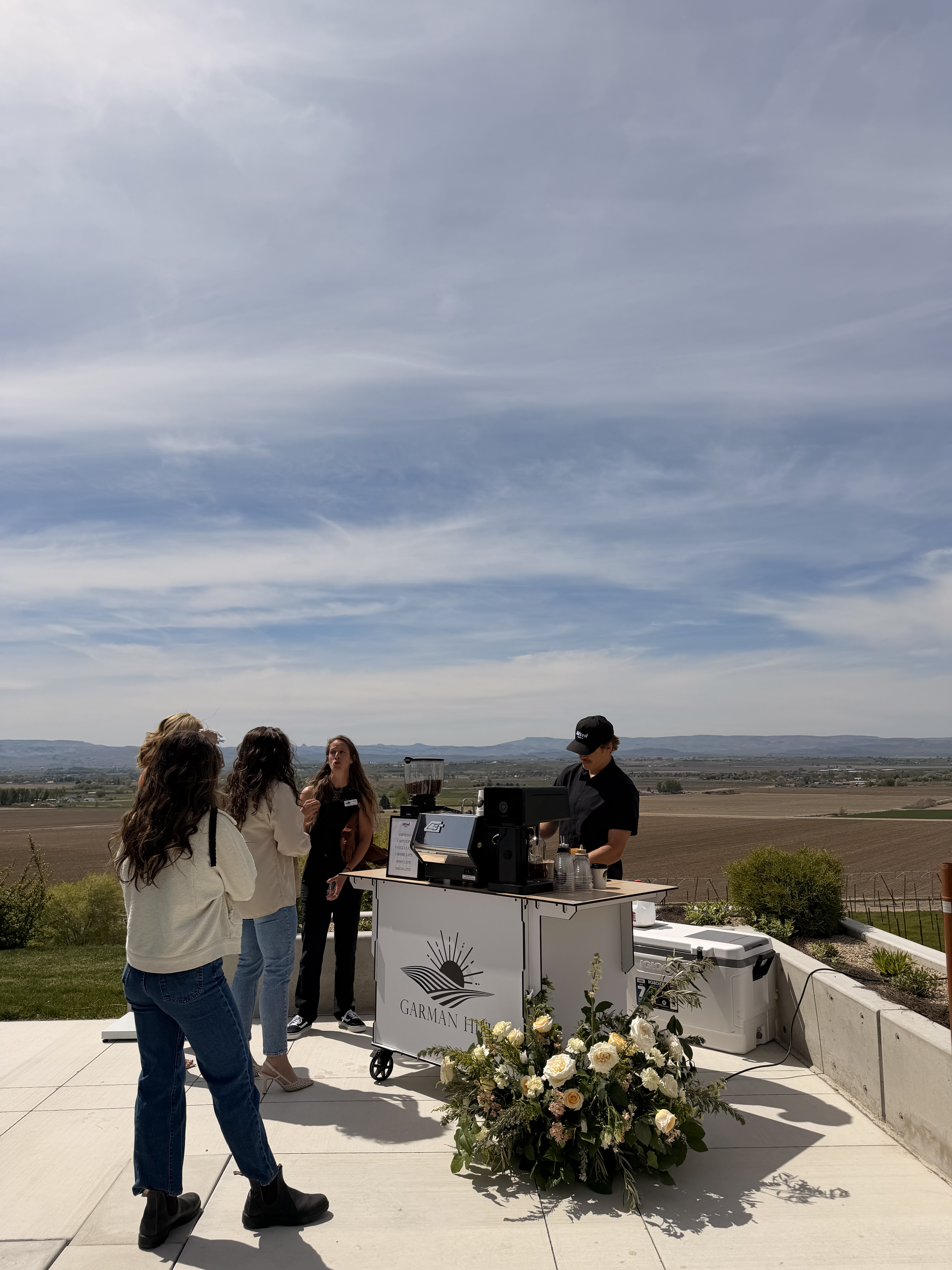 Lifted Coffee Cart barista serving guests at an outdoor wedding at Garman Hill in Idaho with floral arrangements and valley views
