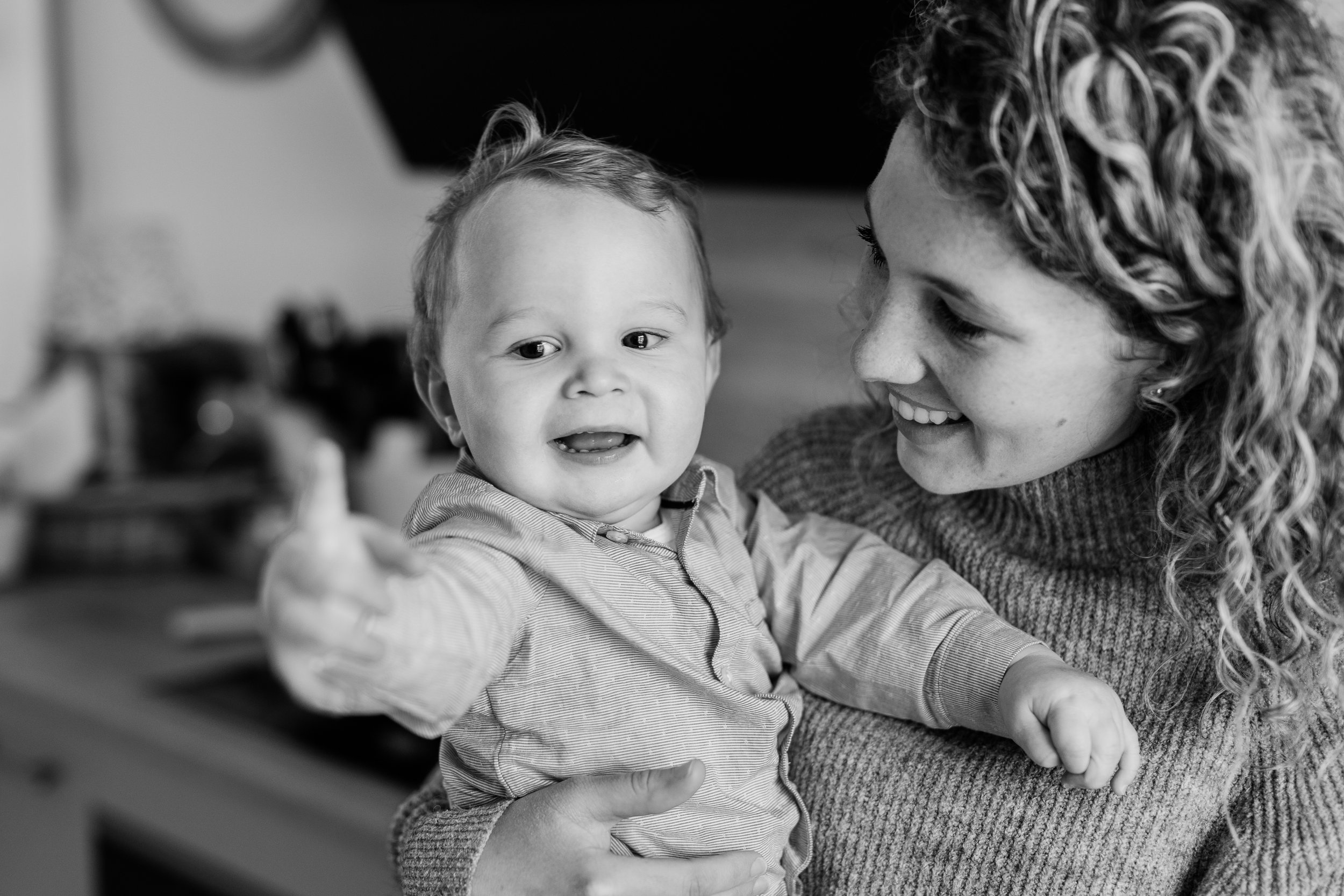 A woman with curly hair smiling while holding a young child with short hair and a striped shirt, both looking at the camera in a black and white photo.