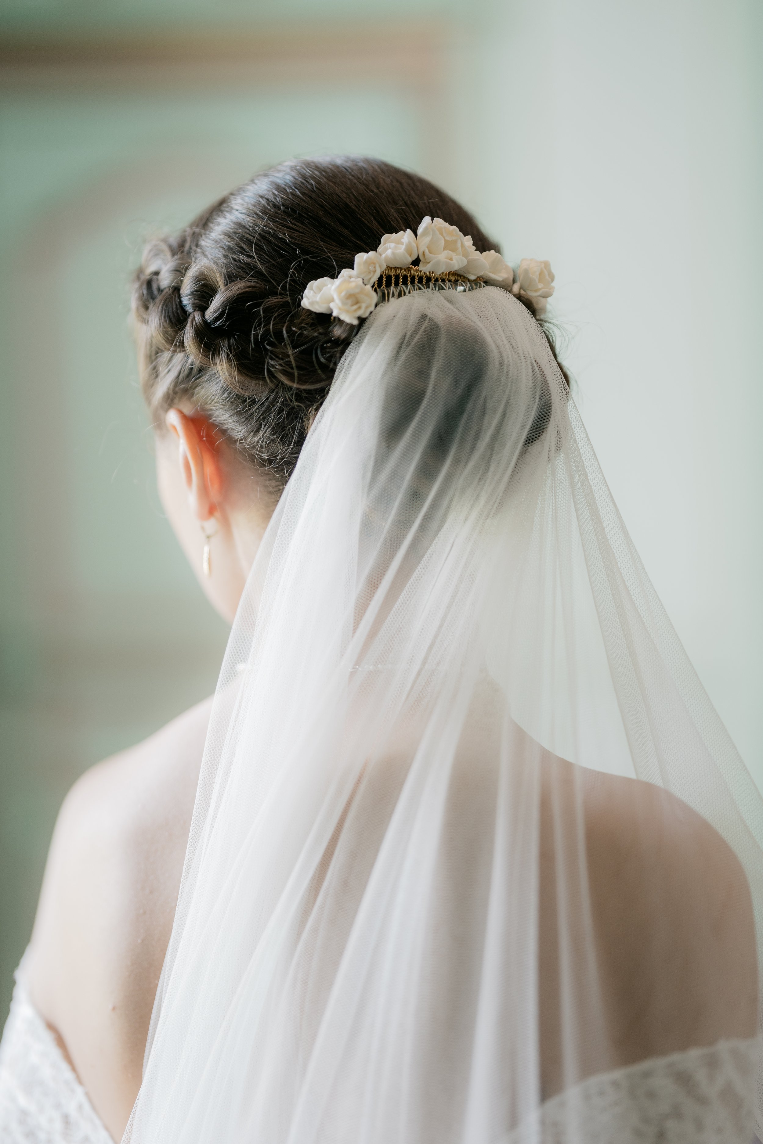 A bride with braided hair, wearing a floral headpiece, and a white veil, viewed from behind.