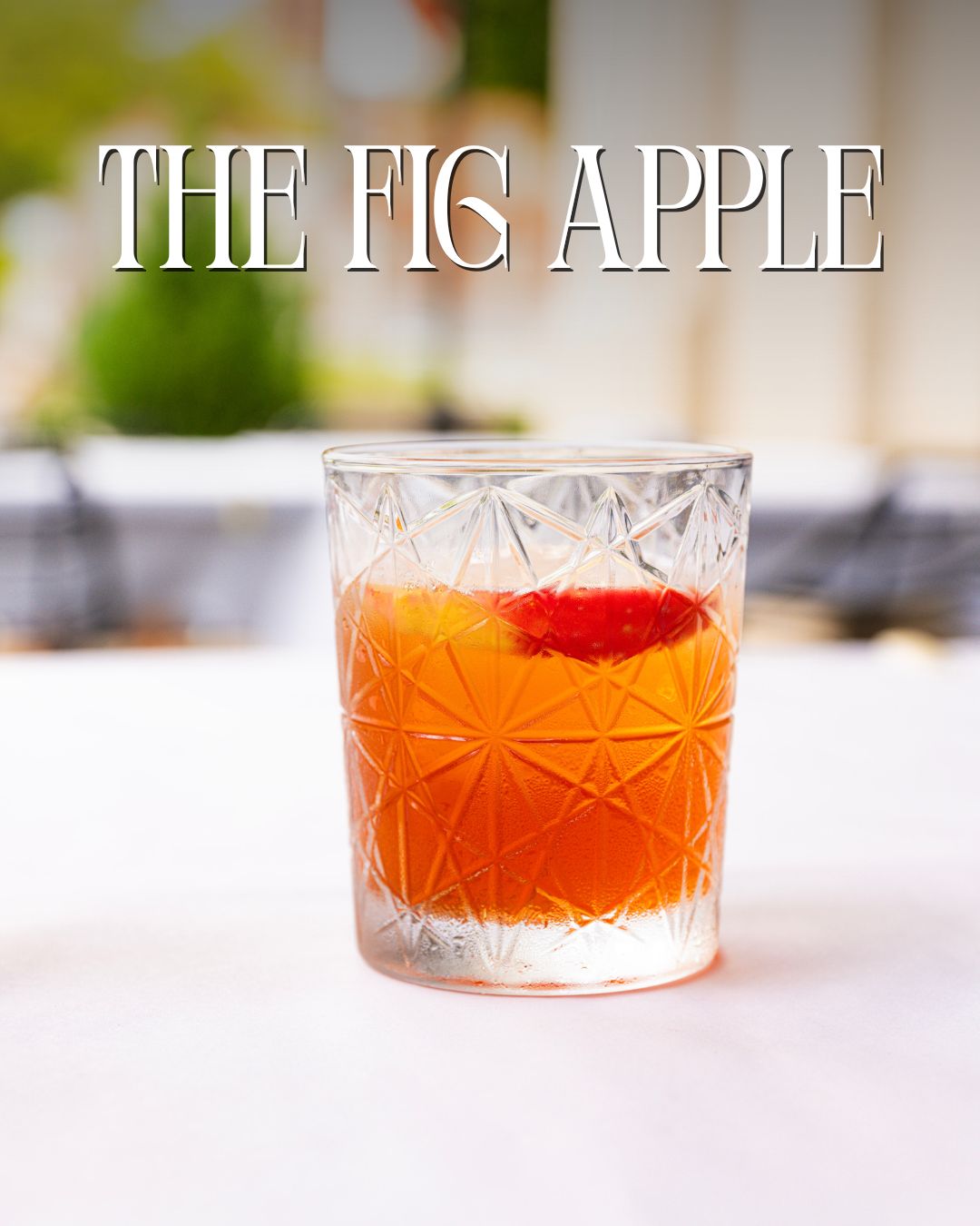 A glass with a geometric pattern containing an orange-colored drink with a cherry and an orange slice, with the text 'The Fig Apple' at the top.